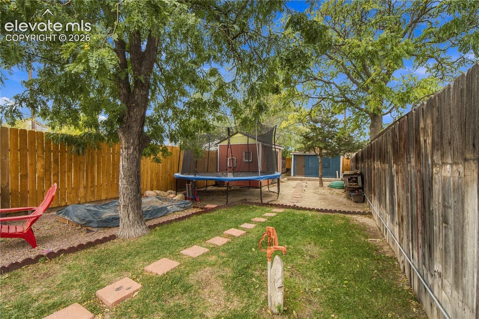 Backyard featuring a wood-fenced perimeter, mature trees, a lawn area with paver stepping stones, and two detached storage structures