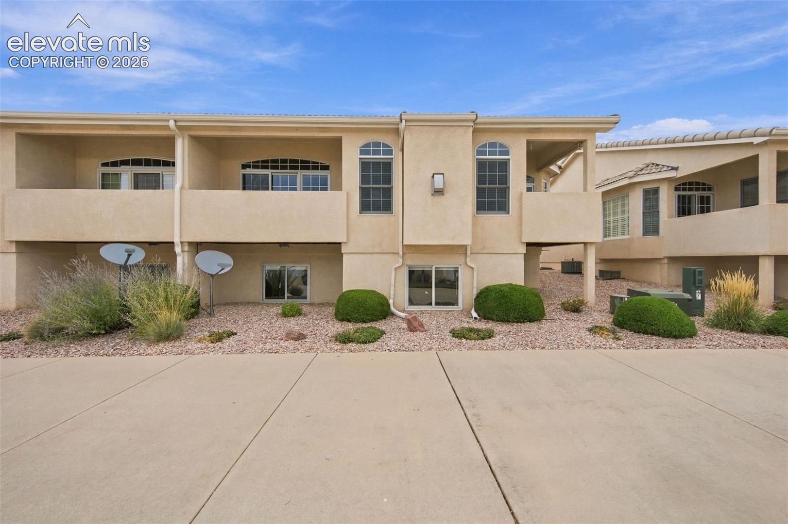 Stucco exterior featuring multi-level balconies, arched window accents, low-maintenance gravel landscaping, and a concrete driveway