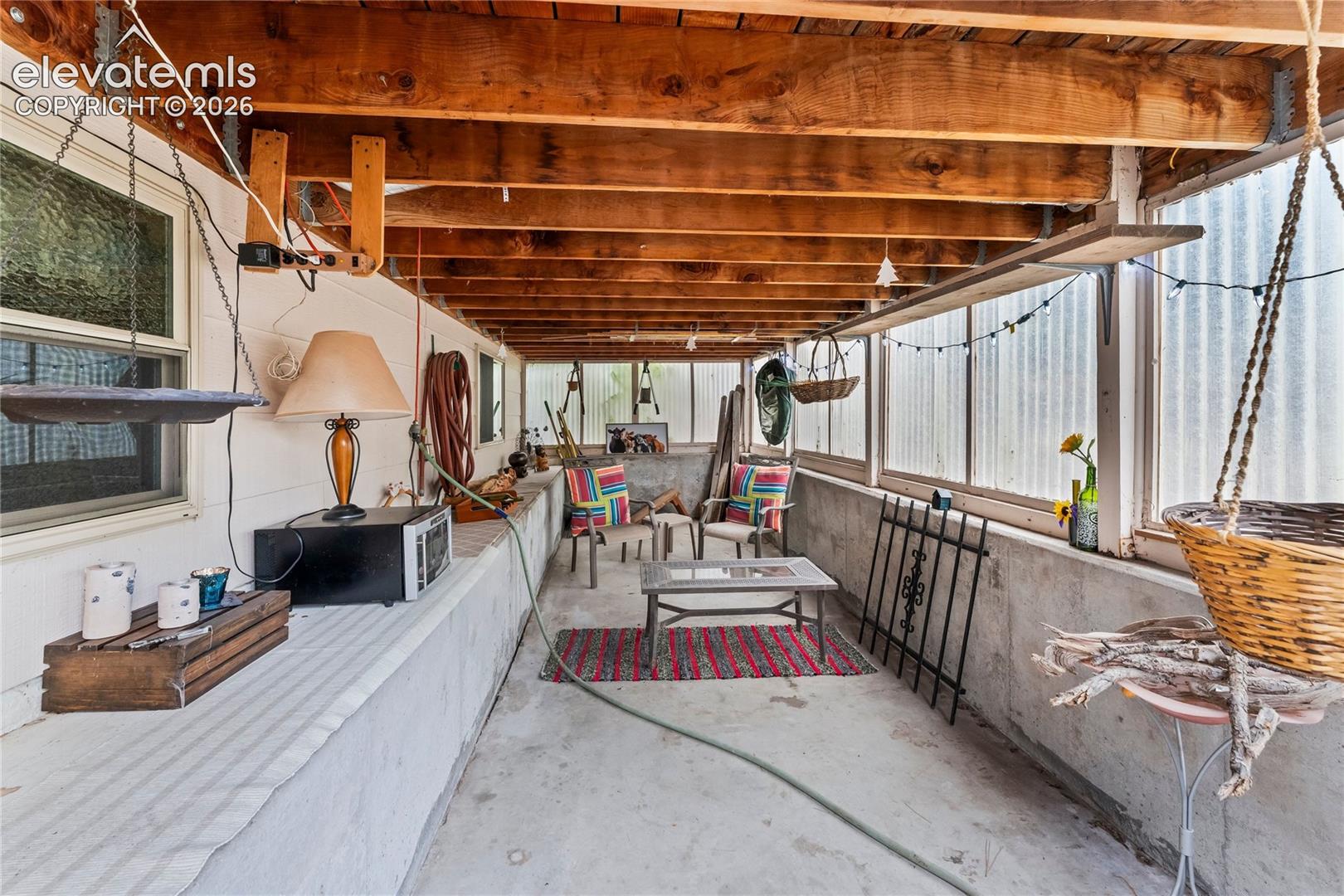 Enclosed patio with exposed wood beam ceiling, concrete flooring, and translucent wall panels providing natural light