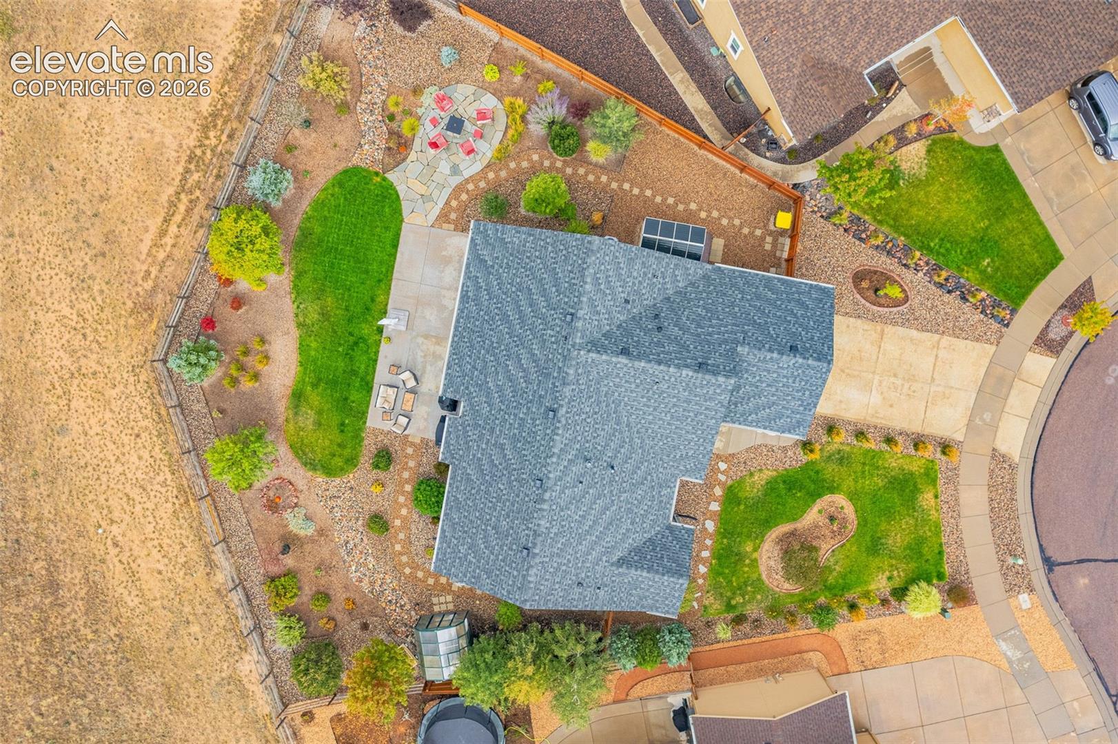 Aerial perspective of residential property featuring a flagstone patio, concrete hardscaping, multiple manicured turf areas, mature landscaping, and wood-style perimeter fencing