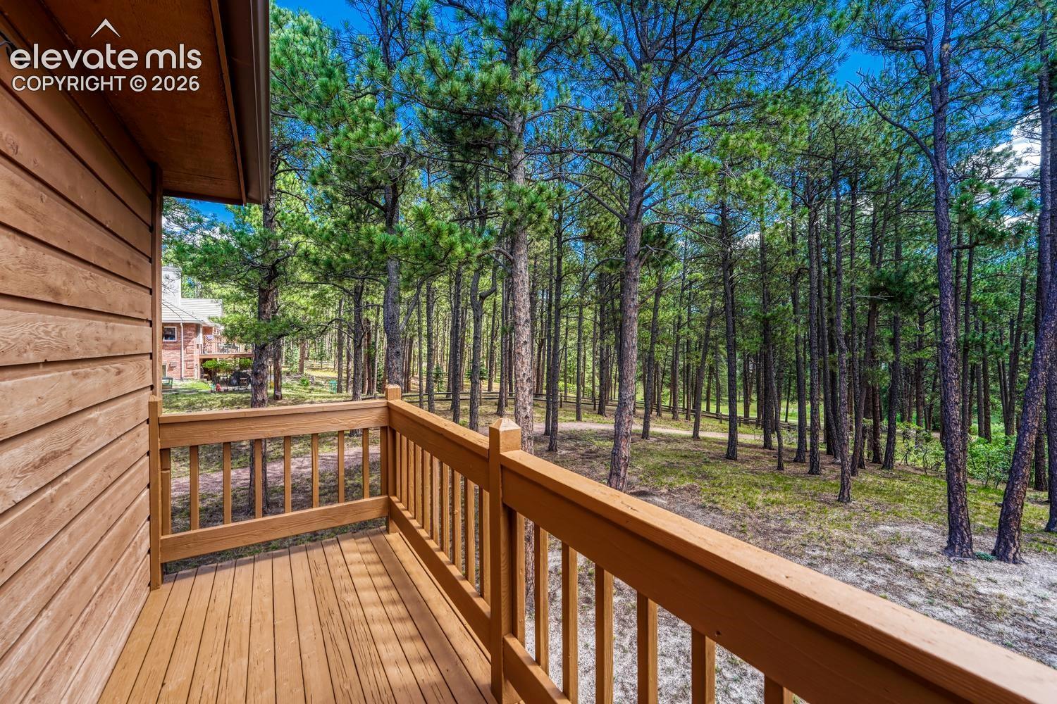 Exterior deck featuring horizontal wood siding, finished wood plank flooring, and a wooden balustrade overlooking a natural forested lot