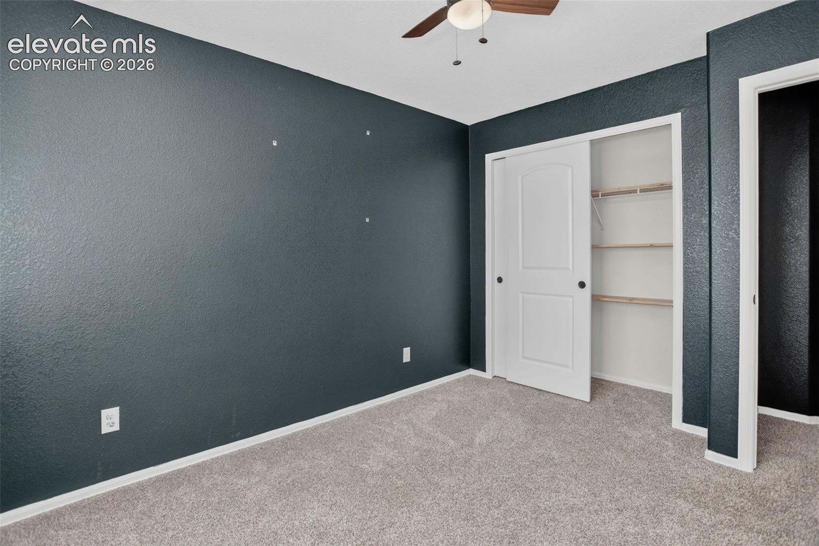 Textured accent wall, ceiling fan, carpet flooring, sliding closet door, built-in closet shelving