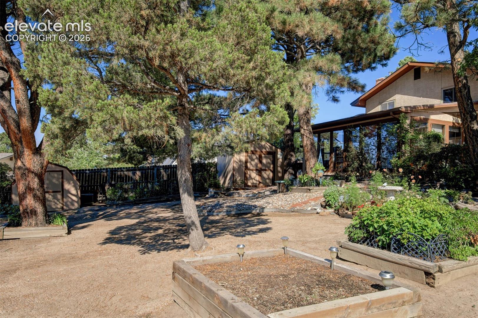 Expansive backyard featuring mature trees, raised planter beds, a storage shed, and a privacy fence