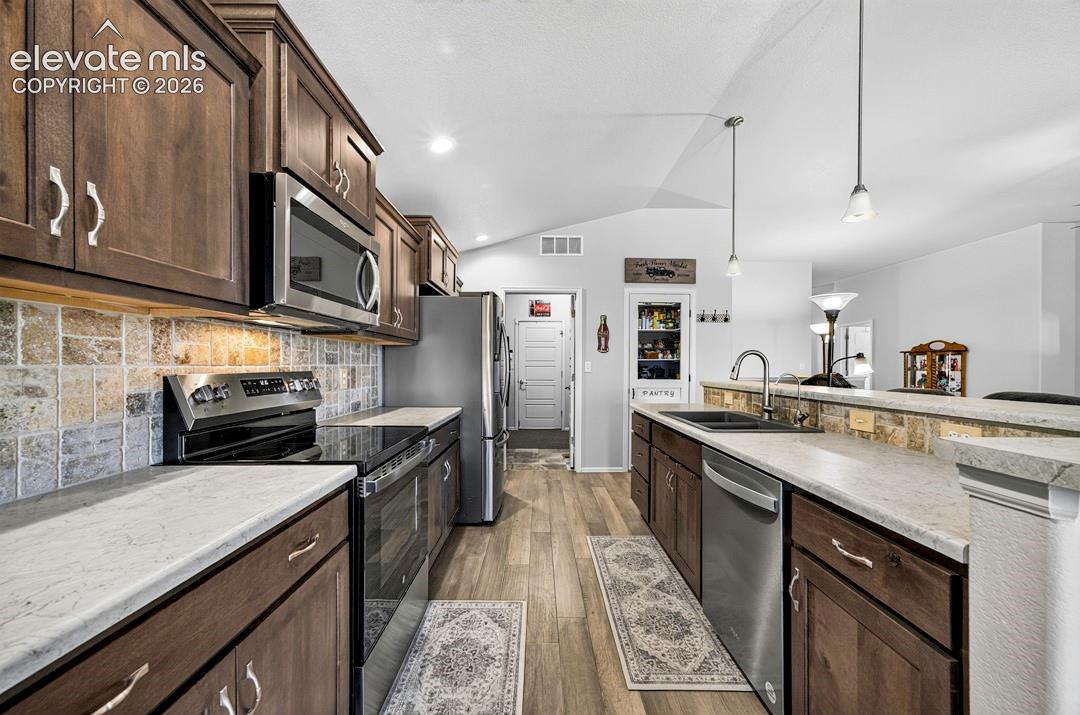 Kitchen featuring wood-finish cabinetry, stainless steel appliances, stone-look countertops, a tiled backsplash, and wood-finish flooring