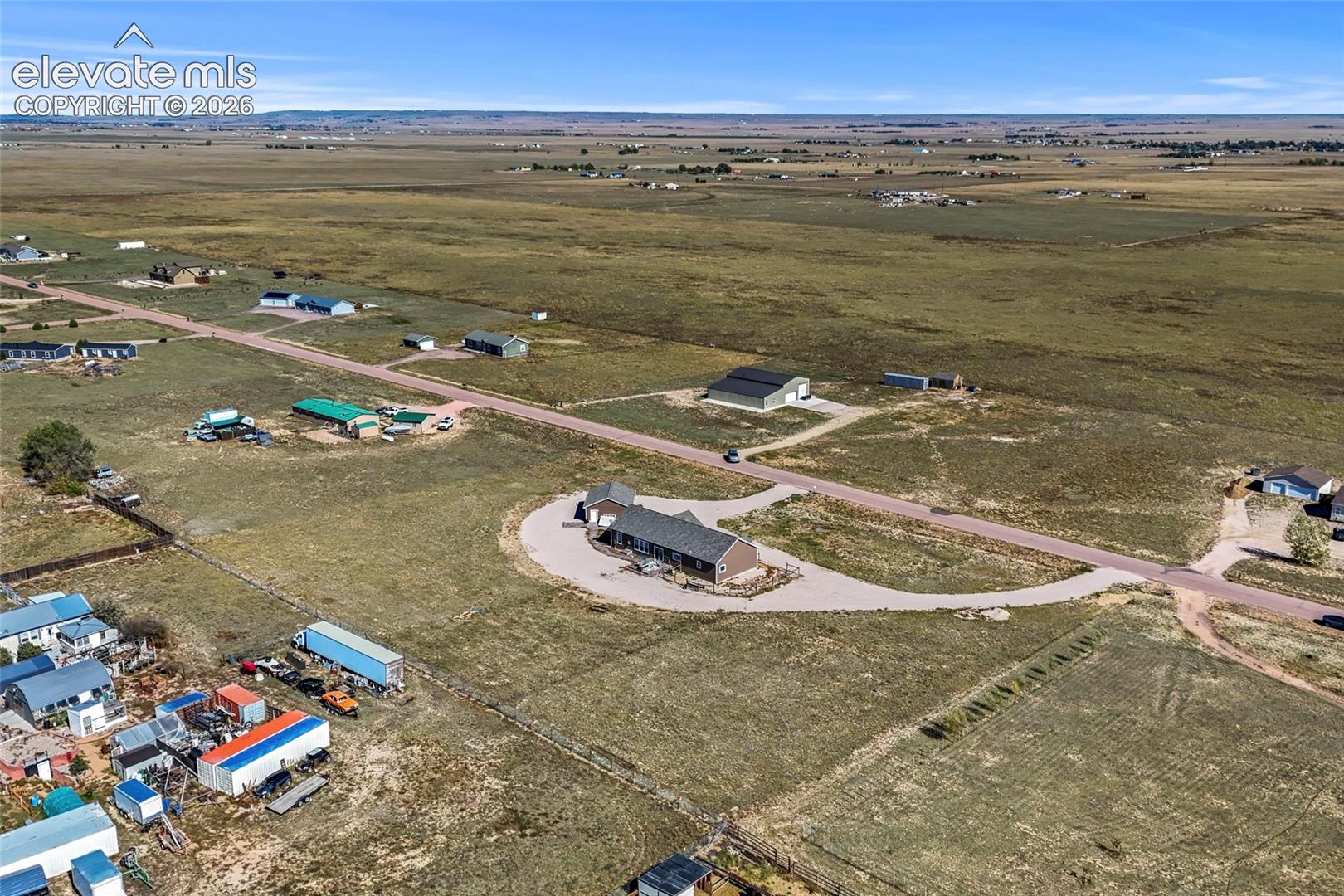 Expansive acreage featuring a single-story residence, a large detached workshop, a circular gravel driveway, and surrounding open plains