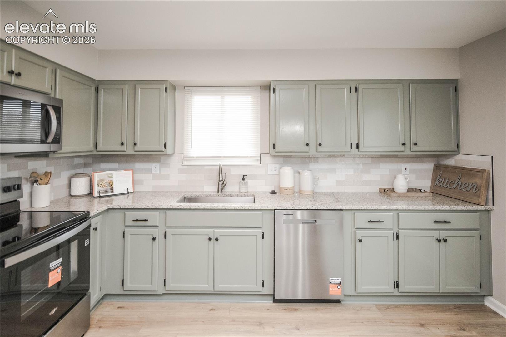 Kitchen featuring shaker-style cabinetry, speckled stone-finish countertops, subway tile backsplash, stainless steel appliances, and wood-finish flooring