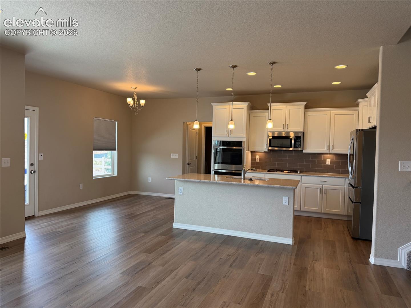 Open-concept living space featuring wood-finish flooring, a kitchen island with pendant lighting, white cabinetry, a tiled backsplash, and stainless steel appliances