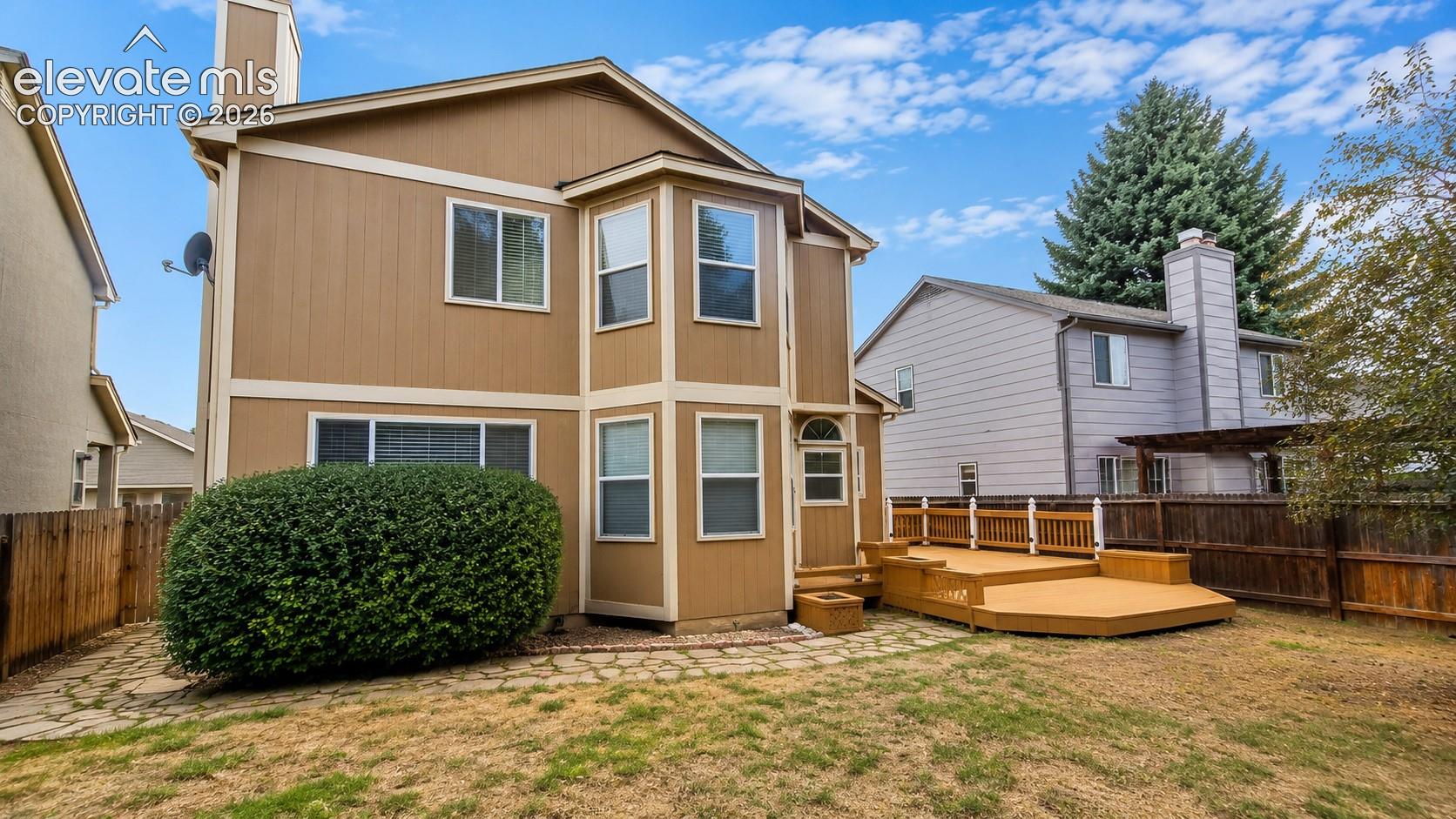 Multi-level wood deck with railing, stone paver pathway, and mature landscaping