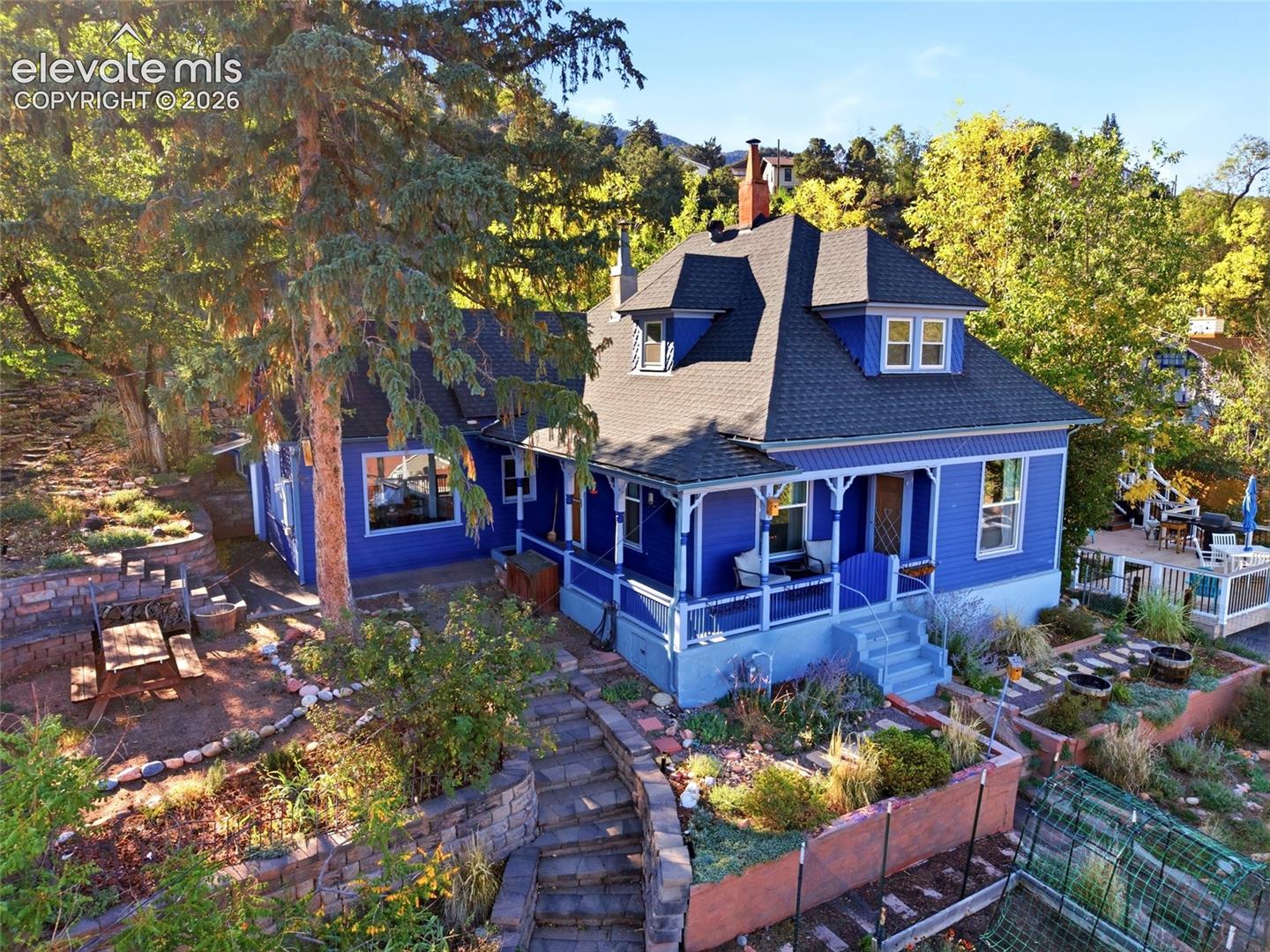 Perched on the high side of the street on Manitou Springs’ beloved Westside, this charming 1905 home offers a rare blend of historic character, unobstructed views, and inviting outdoor living. A welcoming wraparound porch sets the tone, while the elevated setting captures beautiful views through the expansive picture window in the family room, where a wood-burning stove creates a cozy gathering place. Designed for comfortable everyday living, the main level features a primary suite with an attached full bath, convenient laundry with a half bath, and a beautiful custom kitchen that opens to the family room. Granite countertops, stainless steel appliances, soft-close cabinetry, and abundant pullouts combine style with functionality. A separate dining room and an additional living room offer flexibility for entertaining, a library, or a creative retreat. A separate office with its own exterior entrance is ideal for working from home or pursuing a business or creative endeavor. And for a truly distinctive touch, the historic root cellar offers inspiration for a future wine cellar. Recent updates include replacement windows and a tankless water heater. Outside, the approximately 7,500-square-foot lot is a standout, with extensive landscaping, stonework, retaining walls, and thoughtfully designed stairs that create multiple levels of usable space. Enjoy morning coffee on the covered porch or gather with friends in one of the many outdoor sitting areas. A pre-wired hot tub area offers even more possibilities. With no immediate neighbors behind, the setting invites you to slow down and enjoy the birdsong, local wildlife, and peaceful surroundings. Parking is another welcome bonus, with an off-street parking space and on-street parking permits. Upstairs, a charming, light, and airy bedroom features an adjoining bathroom with a classic clawfoot tub and a walk-in closet. Additional unfinished space on this level offers exciting potential for future expansion. All this, just a stroll from Manitou Ave and the dining, shopping, and entertainment that make Manitou Springs so special. Rich in character, full of possibilities, and surrounded by beautiful outdoor spaces, this Westside gem offers a unique opportunity to experience the charm of historic Manitou living.