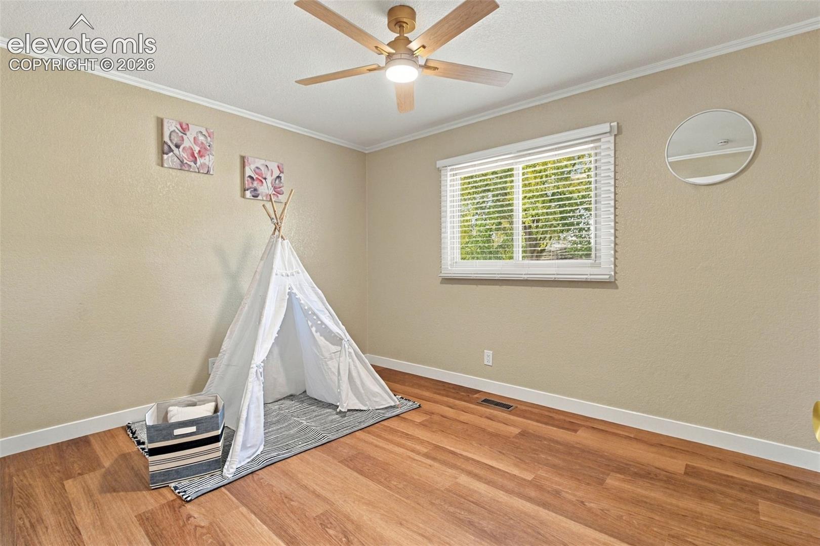 Room featuring wood-finish flooring, a ceiling fan with integrated lighting, and a horizontal window with adjustable blinds