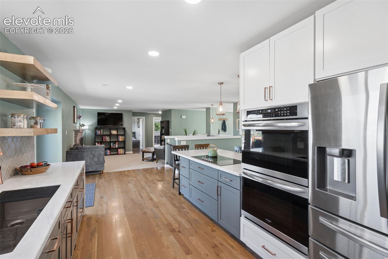 Kitchen featuring white upper cabinetry, blue lower cabinetry, stainless steel double wall ovens, quartz countertops, and wood-finish flooring