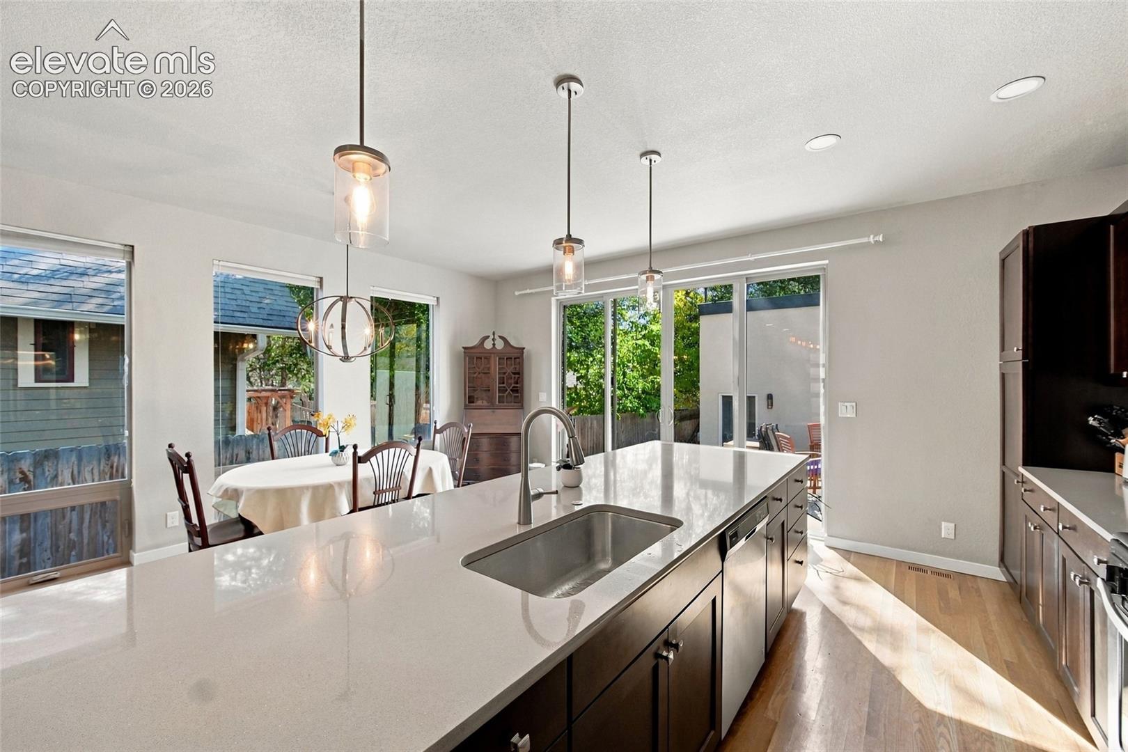 Kitchen featuring a large island with a quartz countertop and stainless steel under-mount sink, dark wood cabinetry, wood-finish flooring, and pendant lighting