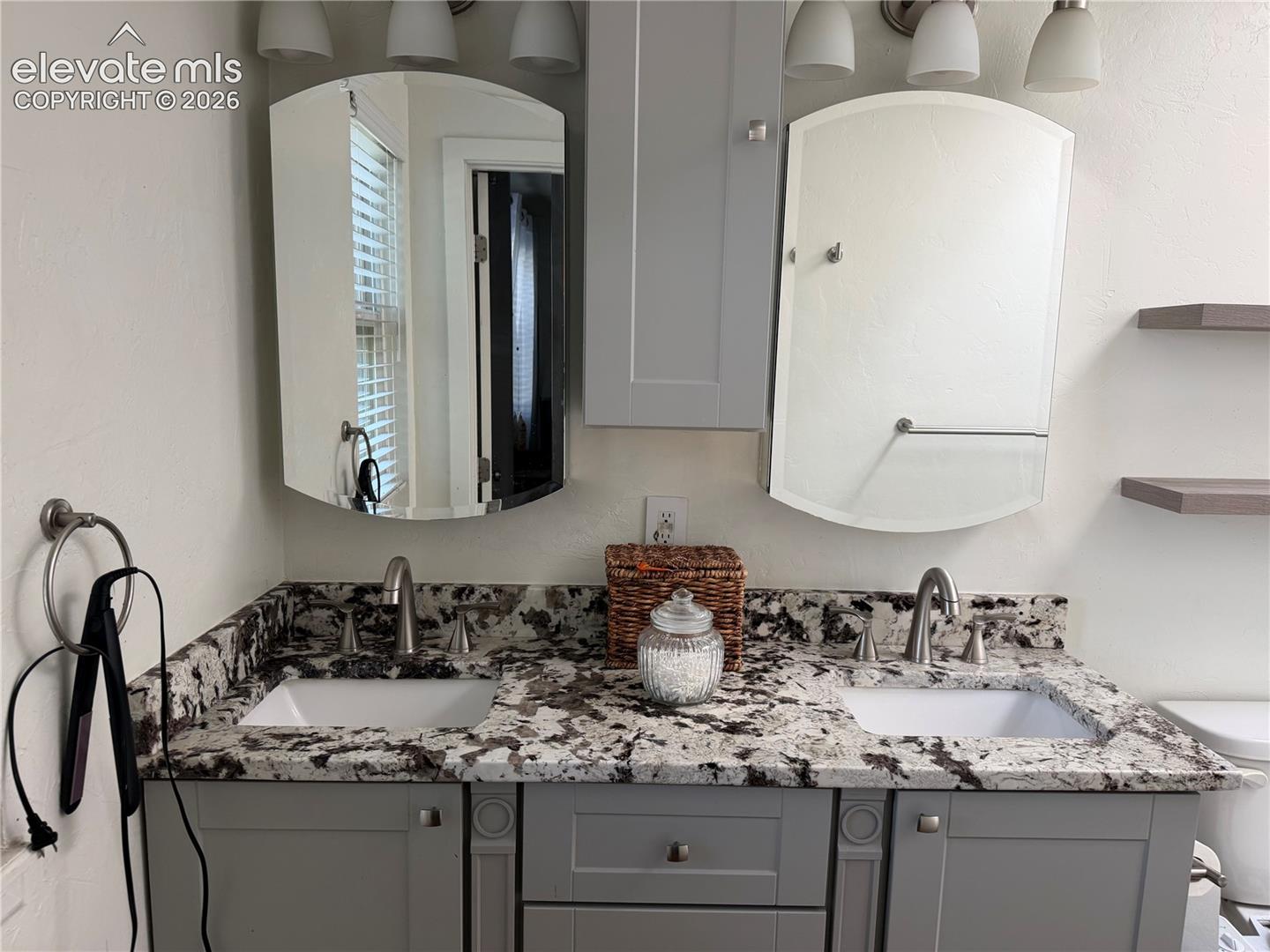 Dual vanity with integrated sinks, speckled stone countertop, light gray cabinetry, and two mirrored medicine cabinets