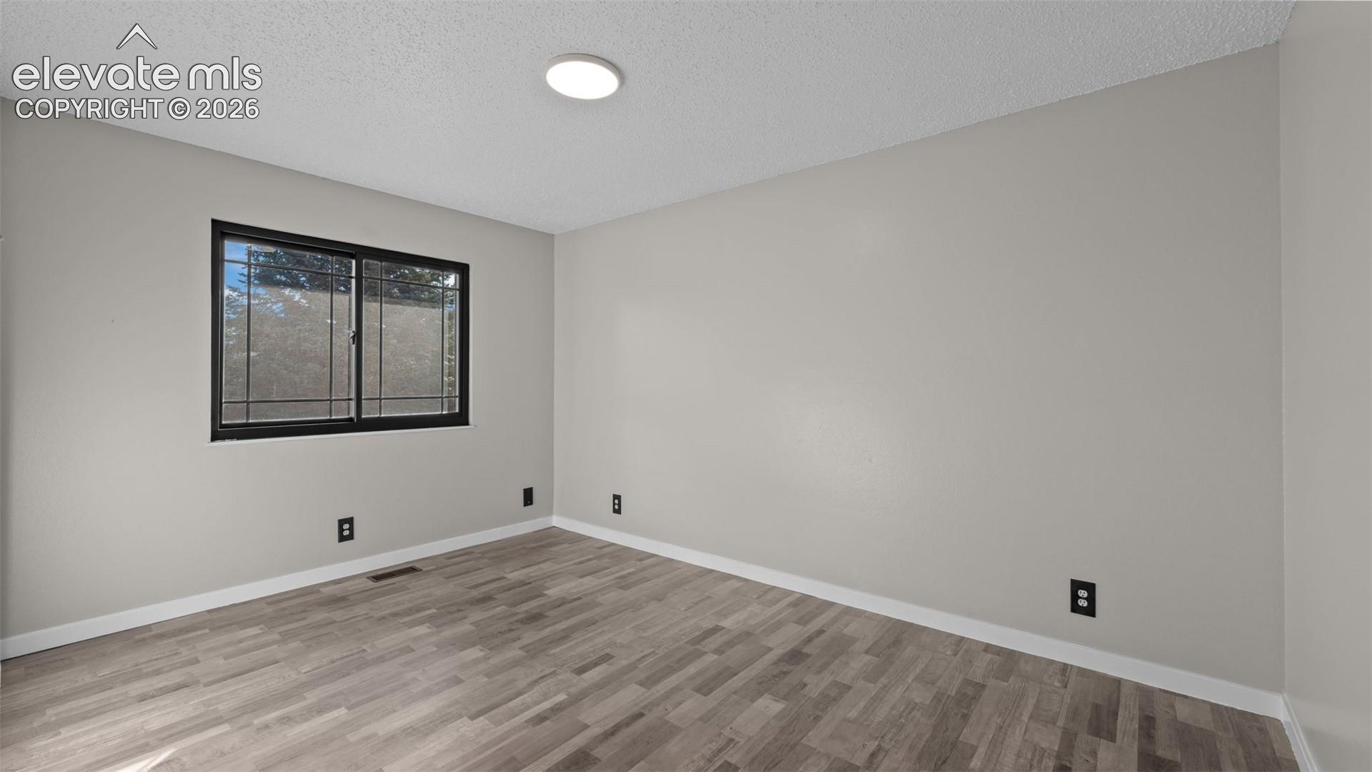 Neutral-toned walls, wood-finish flooring, sliding window with a dark frame, and a flush-mount overhead light fixture