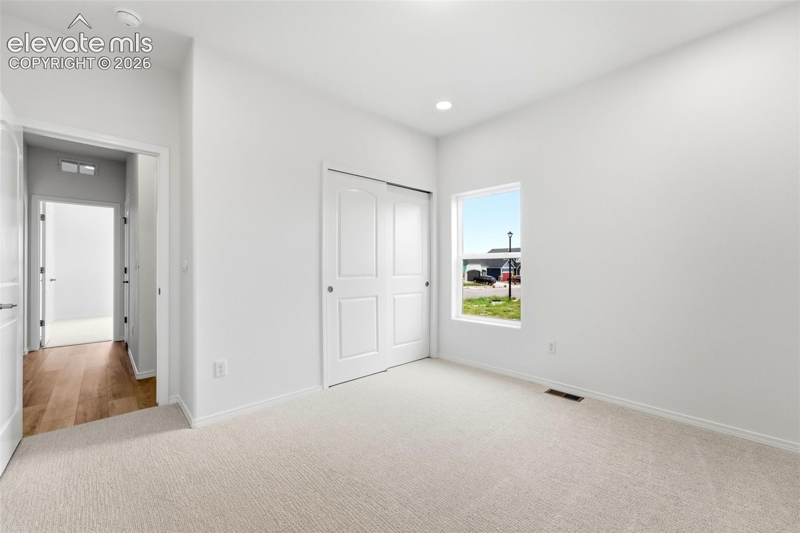 Neutral-toned carpeted room featuring a double-panel closet door, recessed lighting, and a single-pane window