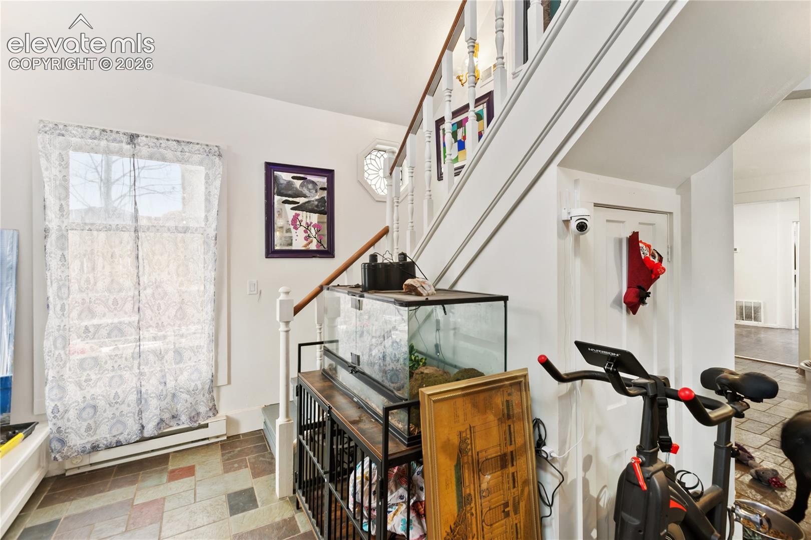 Entryway featuring stone-tile flooring, a staircase with a wooden handrail, and an octagonal accent window