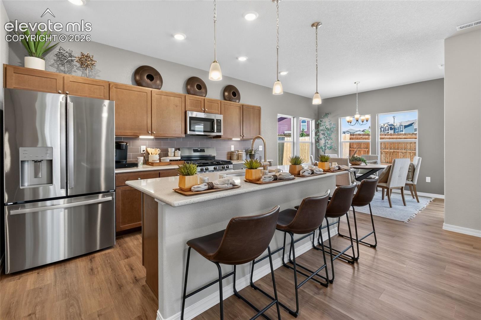 Kitchen featuring wood-finish cabinetry, stone-surface countertop, stainless steel appliances, and pendant lighting over a breakfast bar