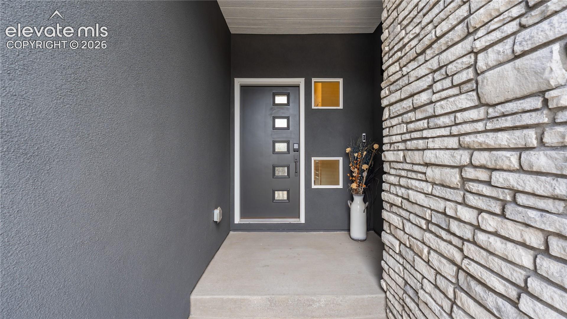 Covered entryway featuring a stacked stone facade, dark grey stucco exterior, and a modern entry door with inset glass panels
