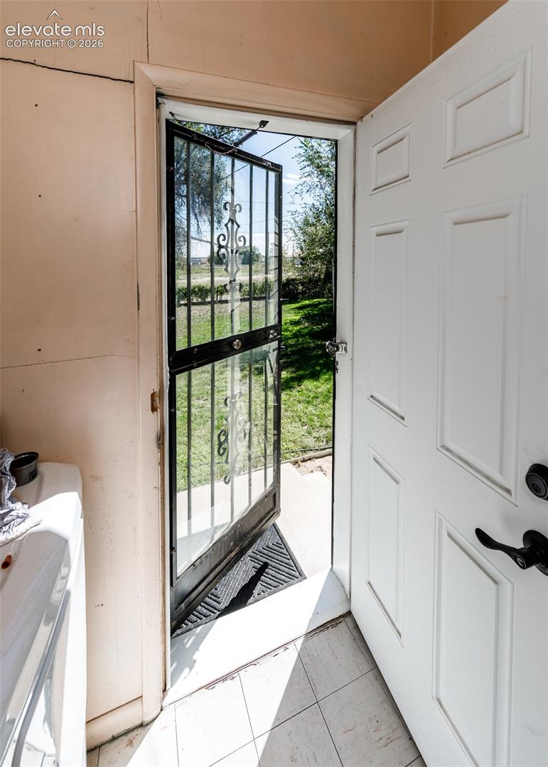 White panel door with a black security screen door, leading to an exterior paved surface and grassy area