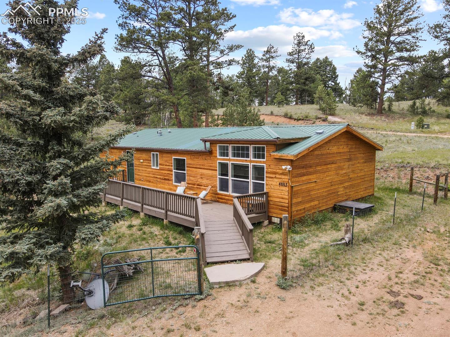 Back of house featuring a deck, a gate, a metal roof, and view of wooded area
