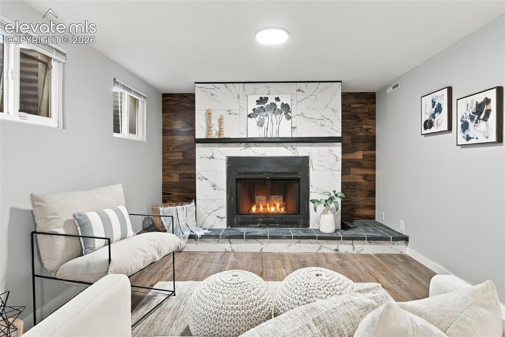 Fireplace featuring stone-finish tiling, dark wood-finish accent paneling, and a raised hearth with wood-finish flooring
