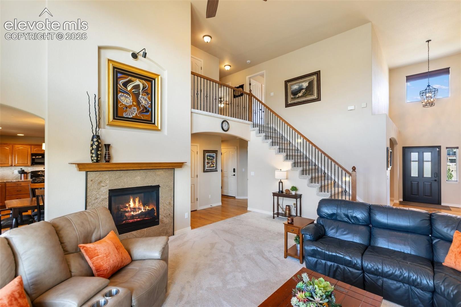 Vaulted ceiling featuring a built-in recessed niche above a stone-surround fireplace with a wood mantel, an open staircase with a metal balustrade, and a multi-pane front door