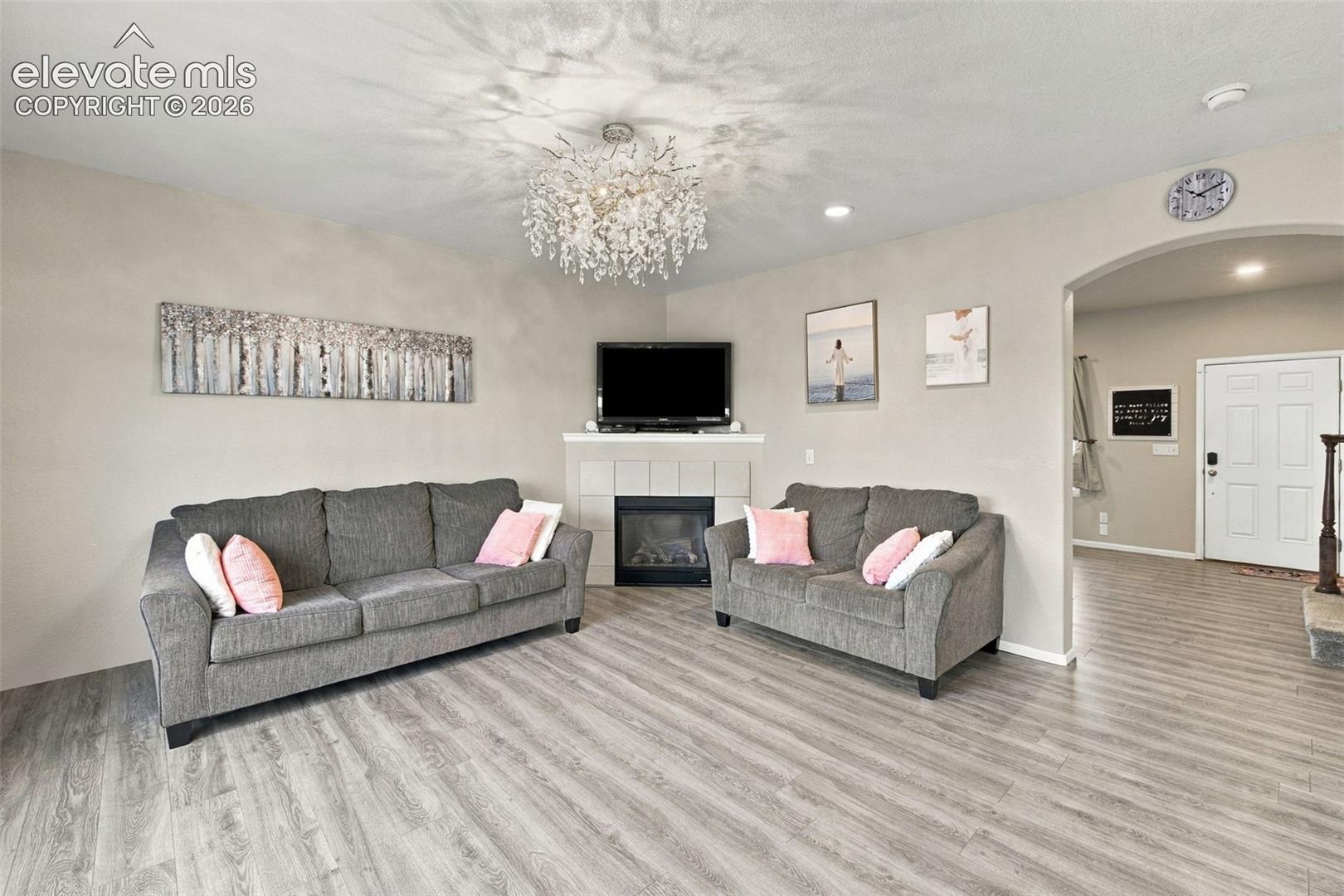 Corner fireplace with tile surround, wood-finish flooring, and multi-light crystal chandelier