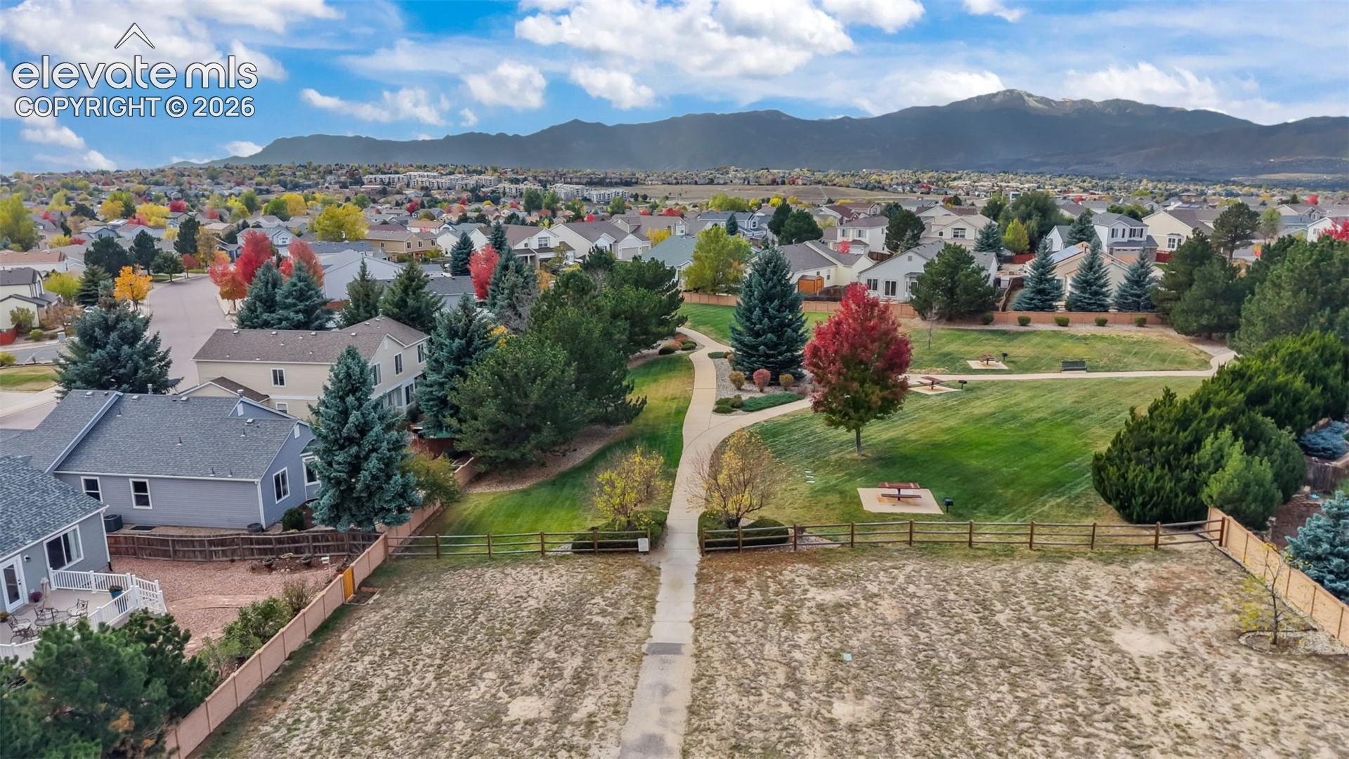 Aerial perspective featuring expansive green space, paved pathways, mature deciduous and coniferous trees, and a mountain range backdrop