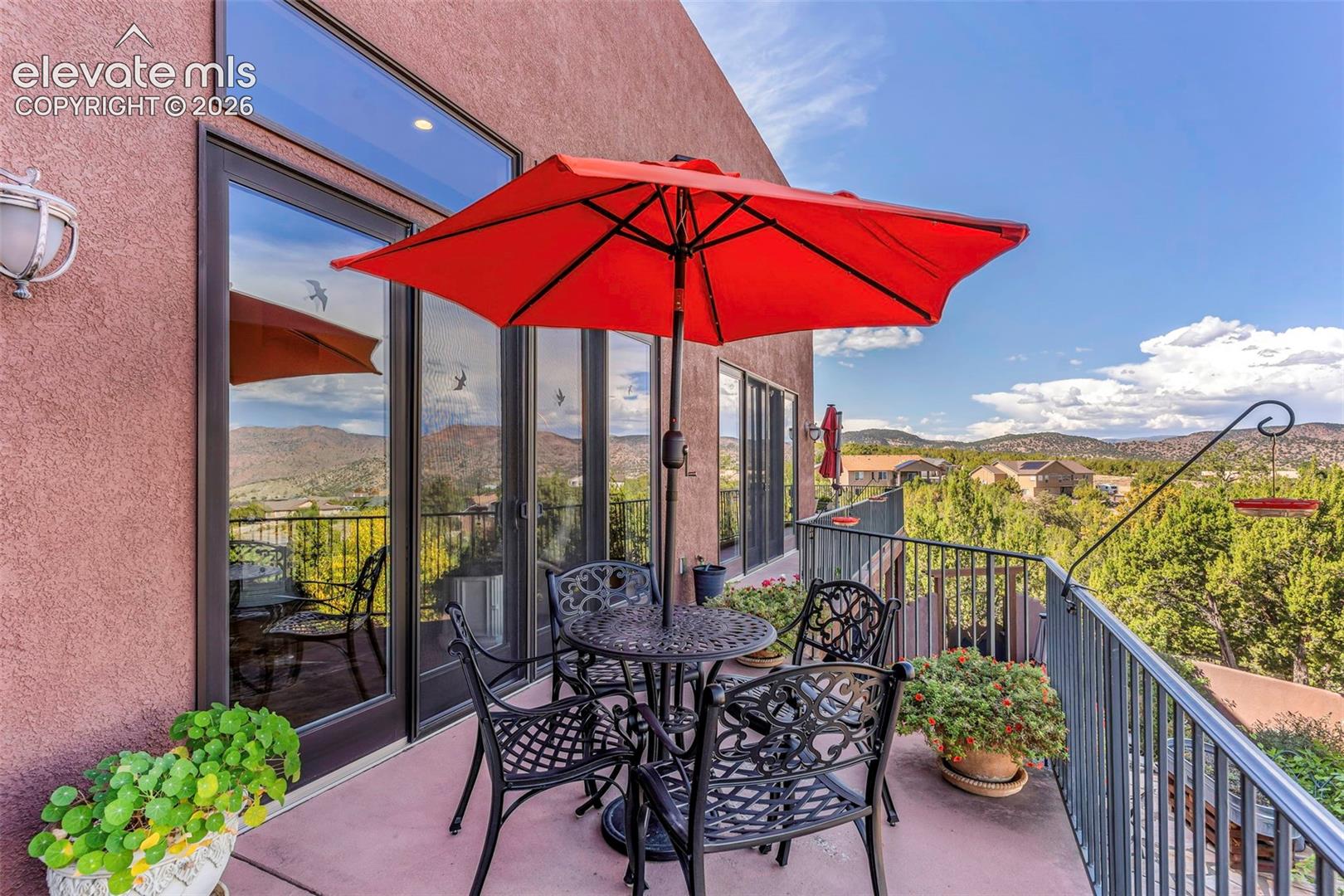 Stucco exterior wall with sliding glass doors, transom windows, and metal railing overlooking a mountain landscape