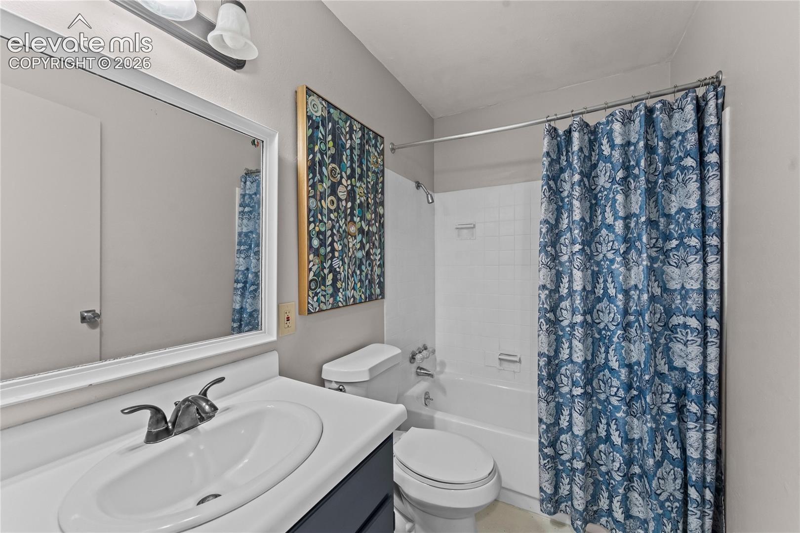 Bathroom featuring a dark-toned vanity with an integrated white sink, a wide-frame wall mirror, an overhead vanity light fixture, and a white porcelain tub-shower combination with tiled surround