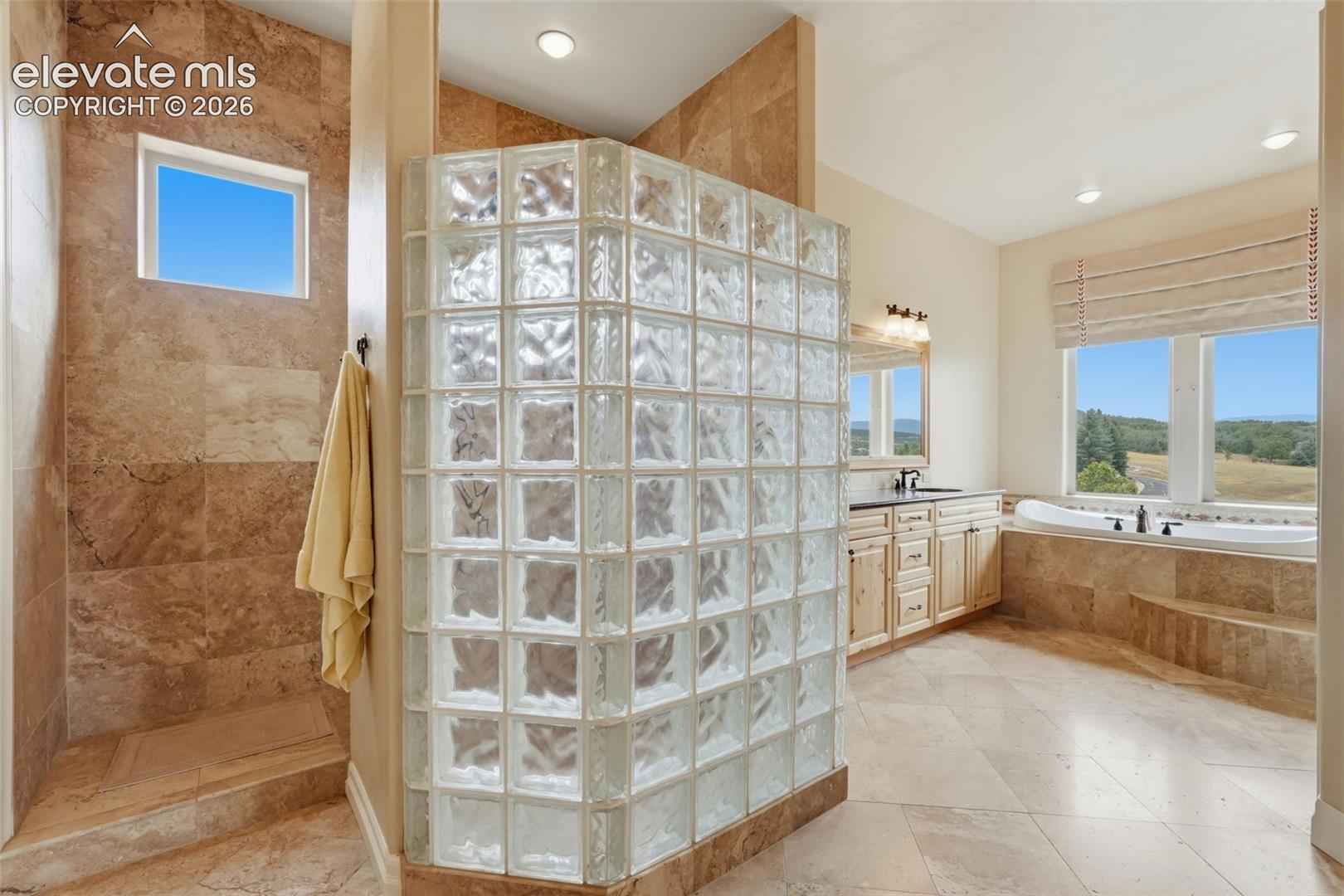 Spacious bathroom featuring a glass block shower enclosure, tiled shower walls, and a separate soaking tub with surrounding tile