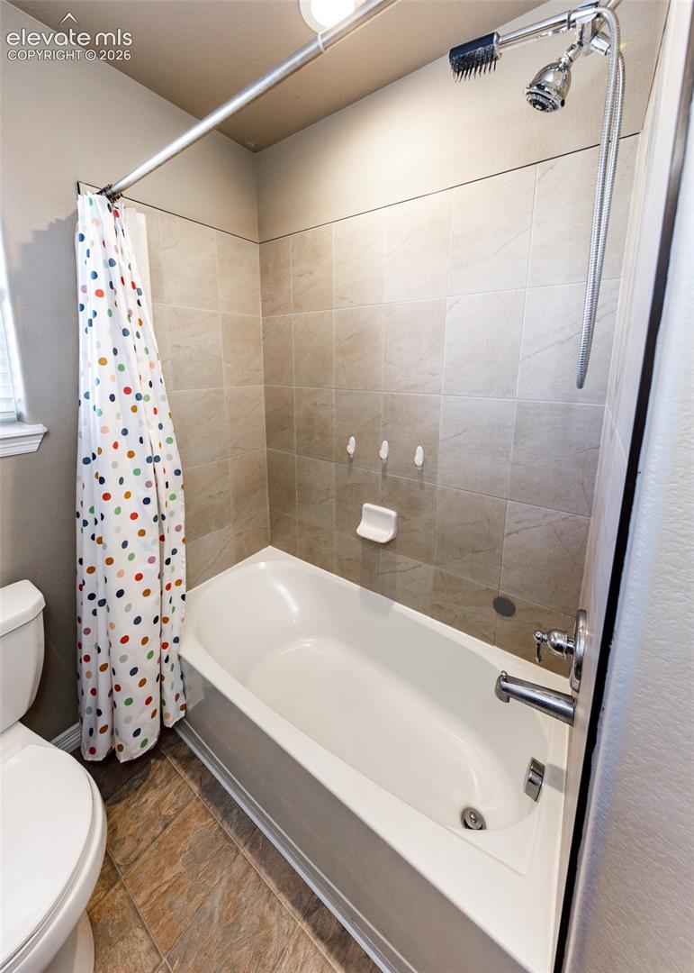 Full-height tub and shower combination featuring neutral square tile surround, chrome faucet assembly, adjustable handheld shower head, and built-in soap dish