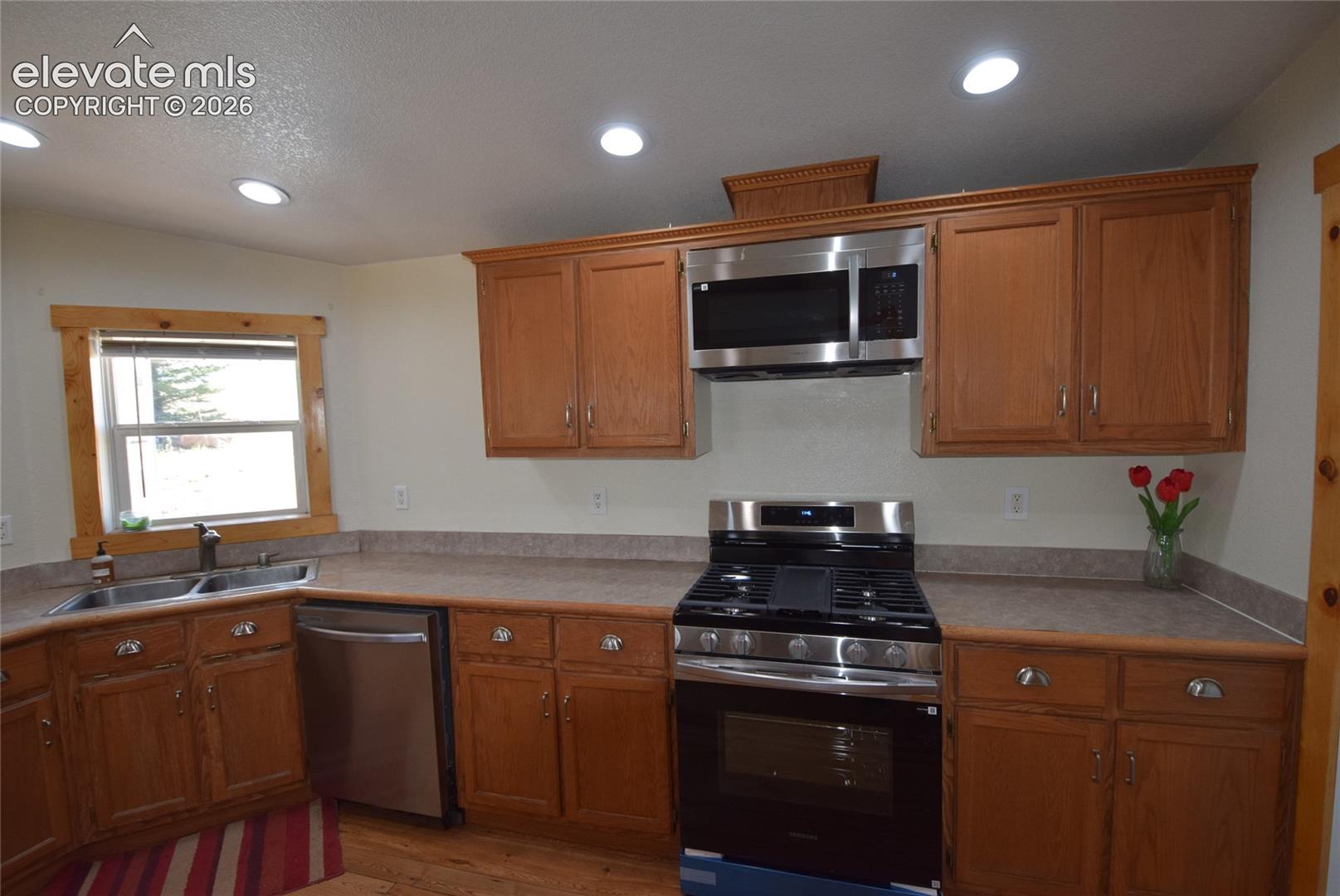 Kitchen featuring recessed lighting, wood-finish cabinetry, stainless steel appliances, and a double basin sink