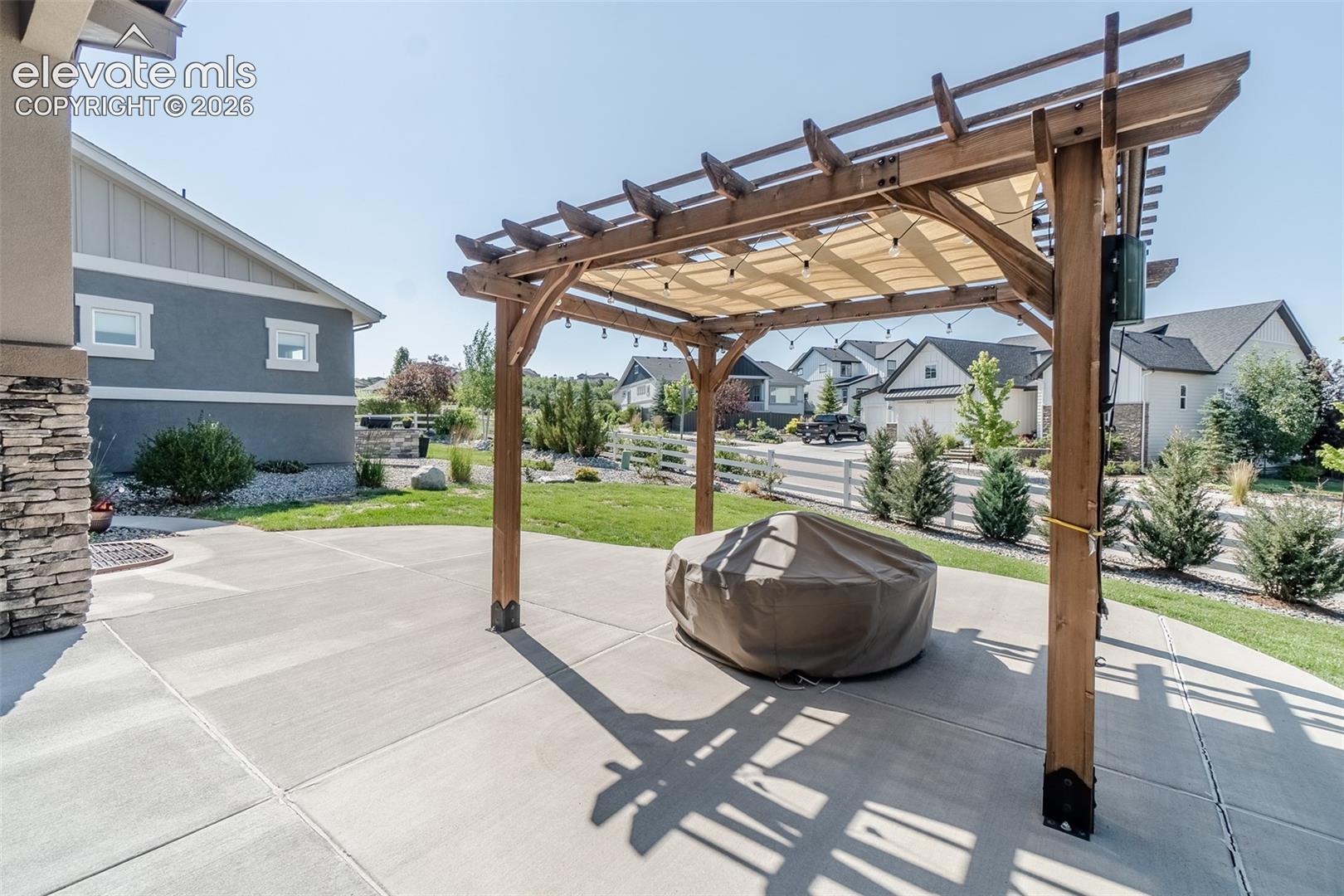 Expansive concrete patio featuring a wooden pergola with a retractable shade canopy and string lighting