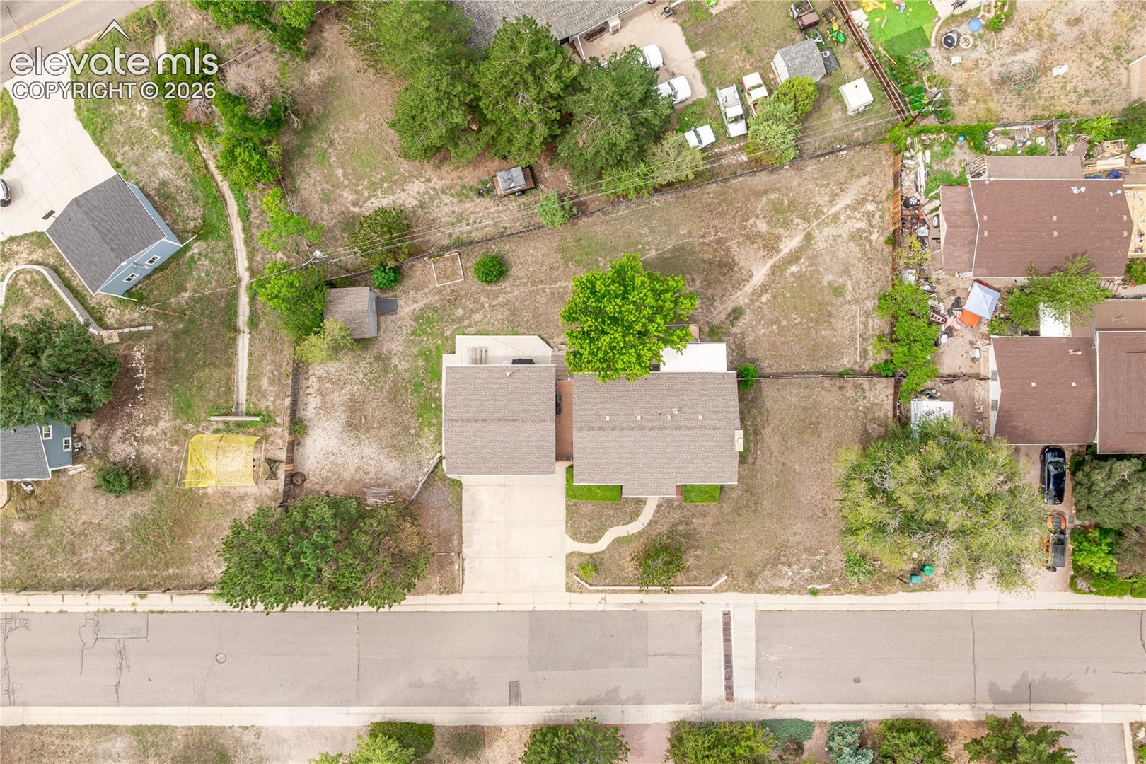 Aerial perspective of a detached residential structure featuring a concrete driveway, a concrete walkway, and expansive outdoor grounds with mature trees