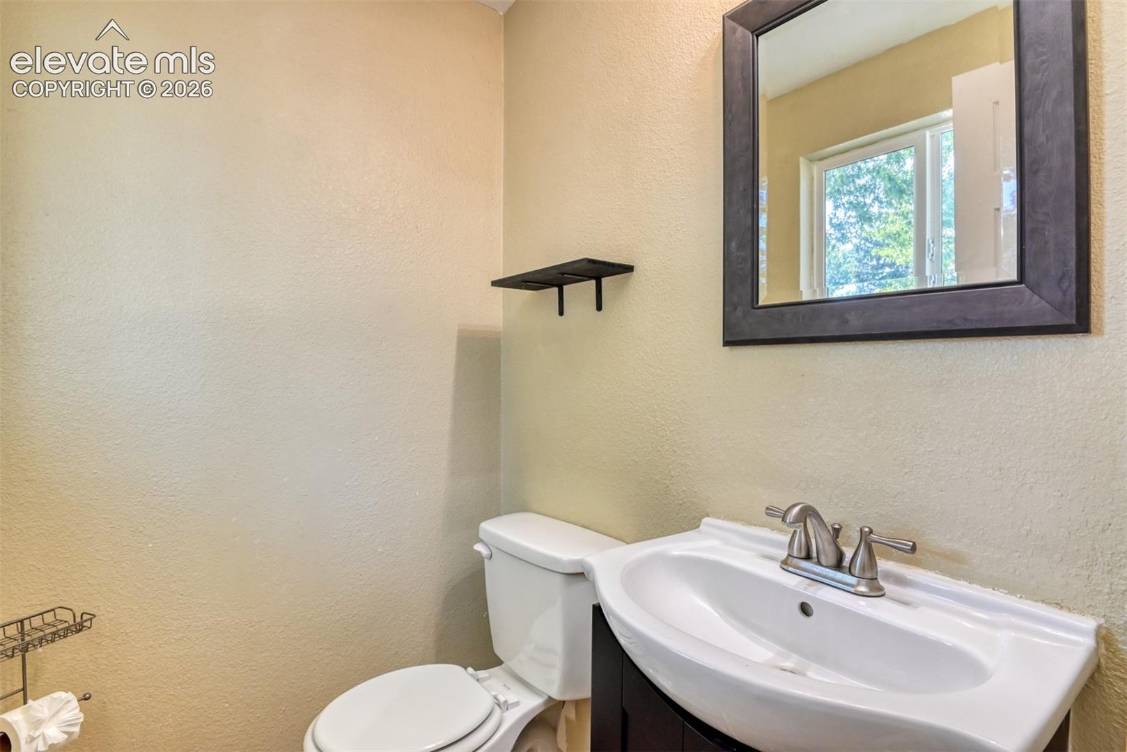 Powder room featuring a dark wood-finish framed mirror, white ceramic sink with brushed nickel faucet, and neutral wall paint