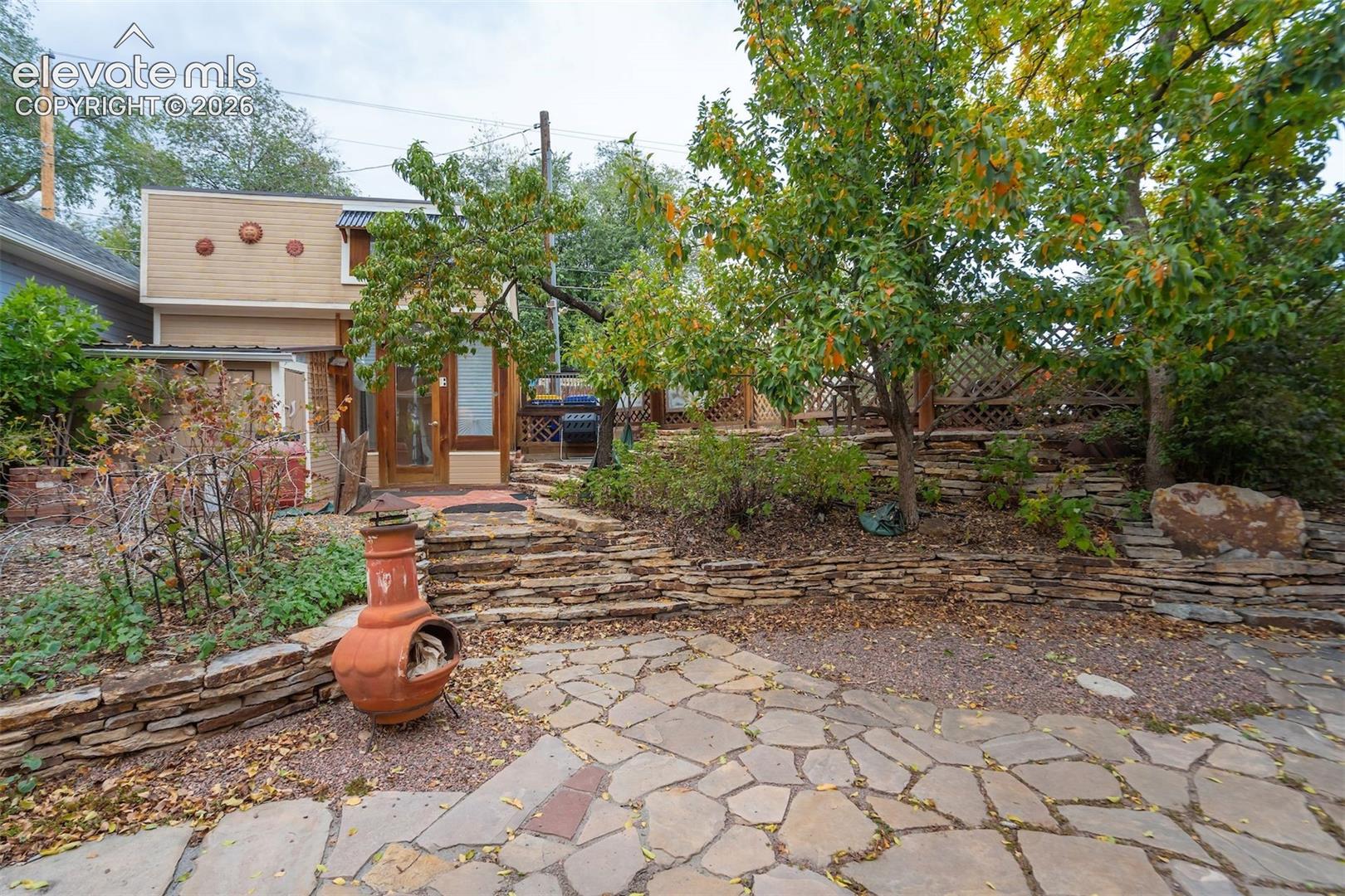 Stone paver patio leading to natural stone steps with stacked stone retaining walls, mature trees, and landscaping