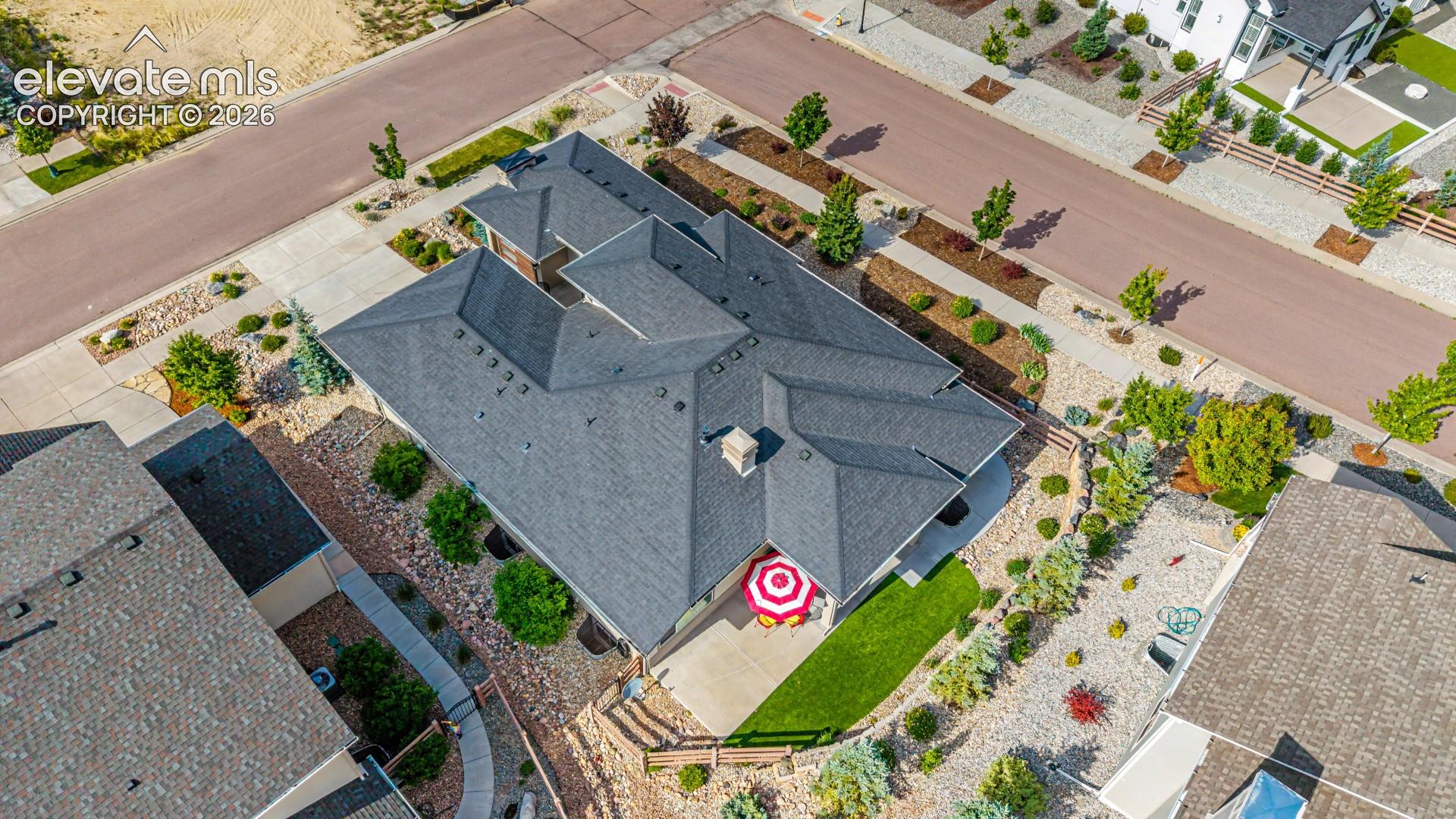 Asphalt shingle roofing, concrete patio, artificial turf, and extensive rock landscaping