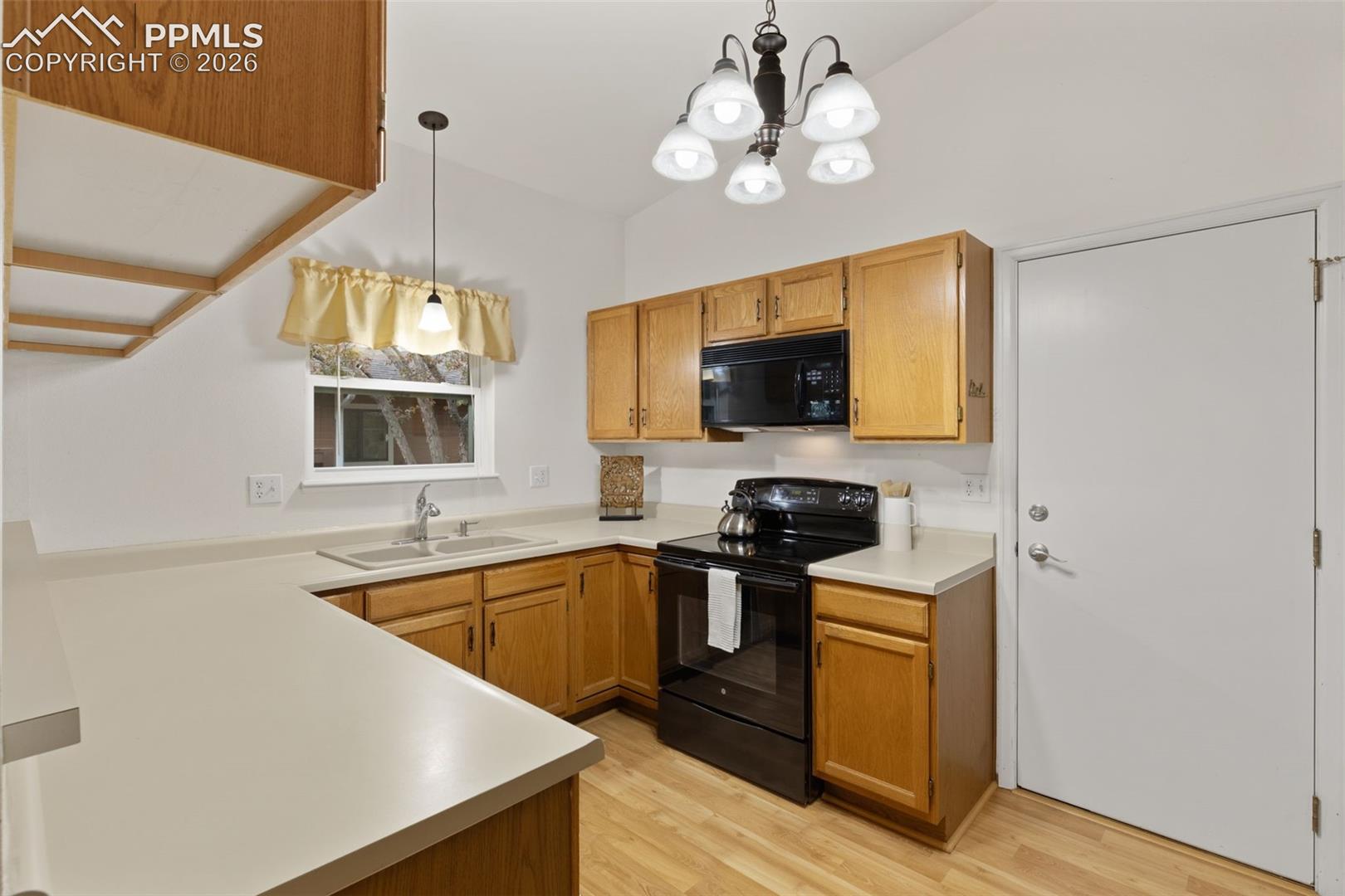 Kitchen features wood cabinetry, light-colored countertops, a double-basin sink, and black appliances including a microwave and range