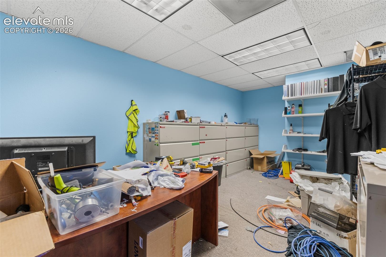 Interior space featuring built-in metal filing cabinetry, wall-mounted shelving units, and a suspended drop ceiling with recessed lighting