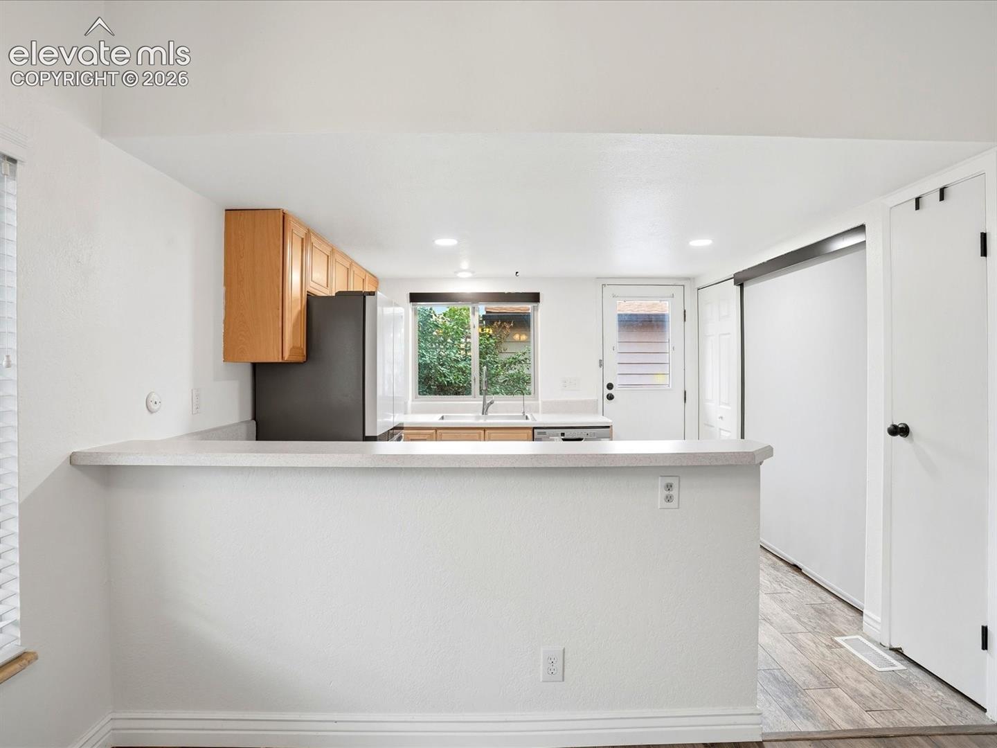 Kitchen featuring wood cabinetry, a pass-through breakfast bar with a solid surface countertop, wood-finish flooring, and a glass-paneled exterior door