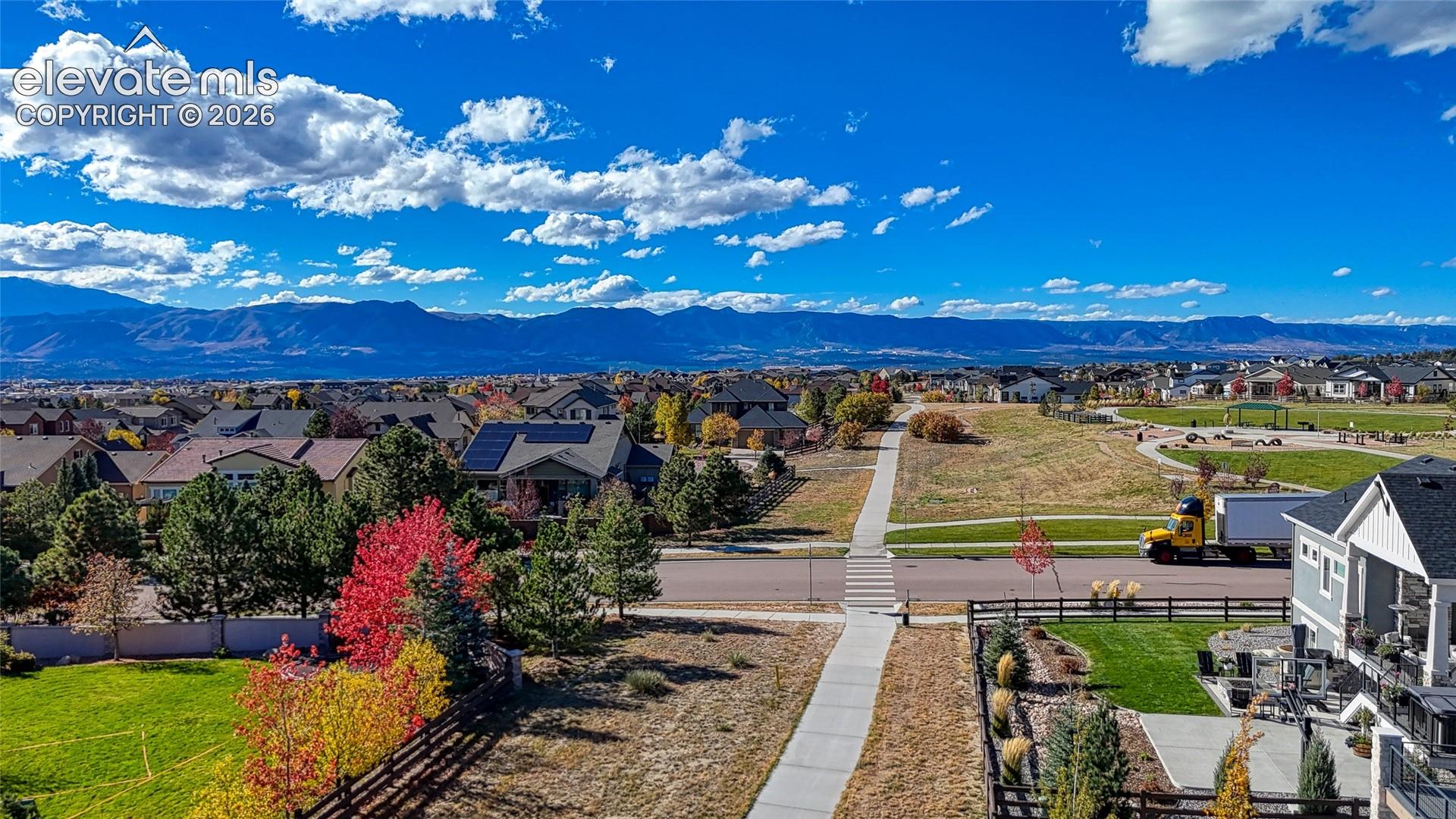 Aerial perspective featuring prominent mountain range backdrop, paved pedestrian pathways, manicured green space, and mature deciduous trees