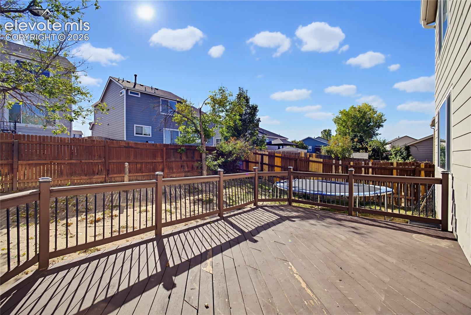 Elevated wood-surface deck with black metal balusters and a perimeter wood privacy fence