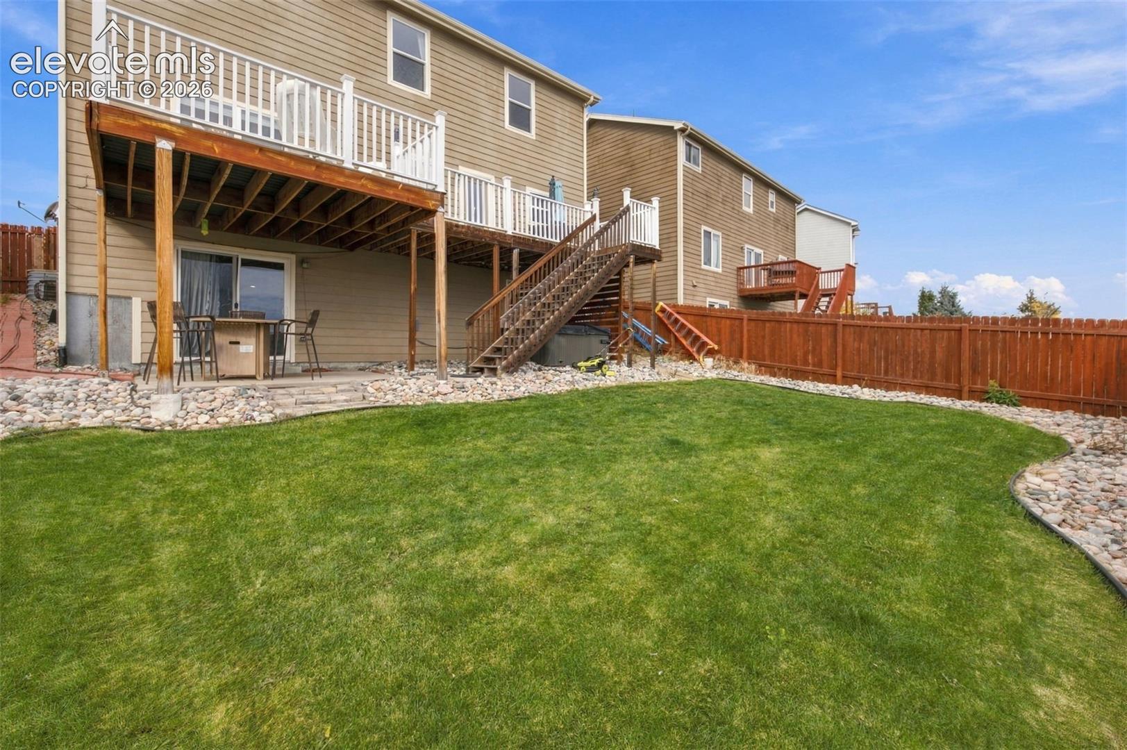 Backyard featuring a elevated wood deck with white railings, stairs to the lawn, rock landscaping, and a wood privacy fence