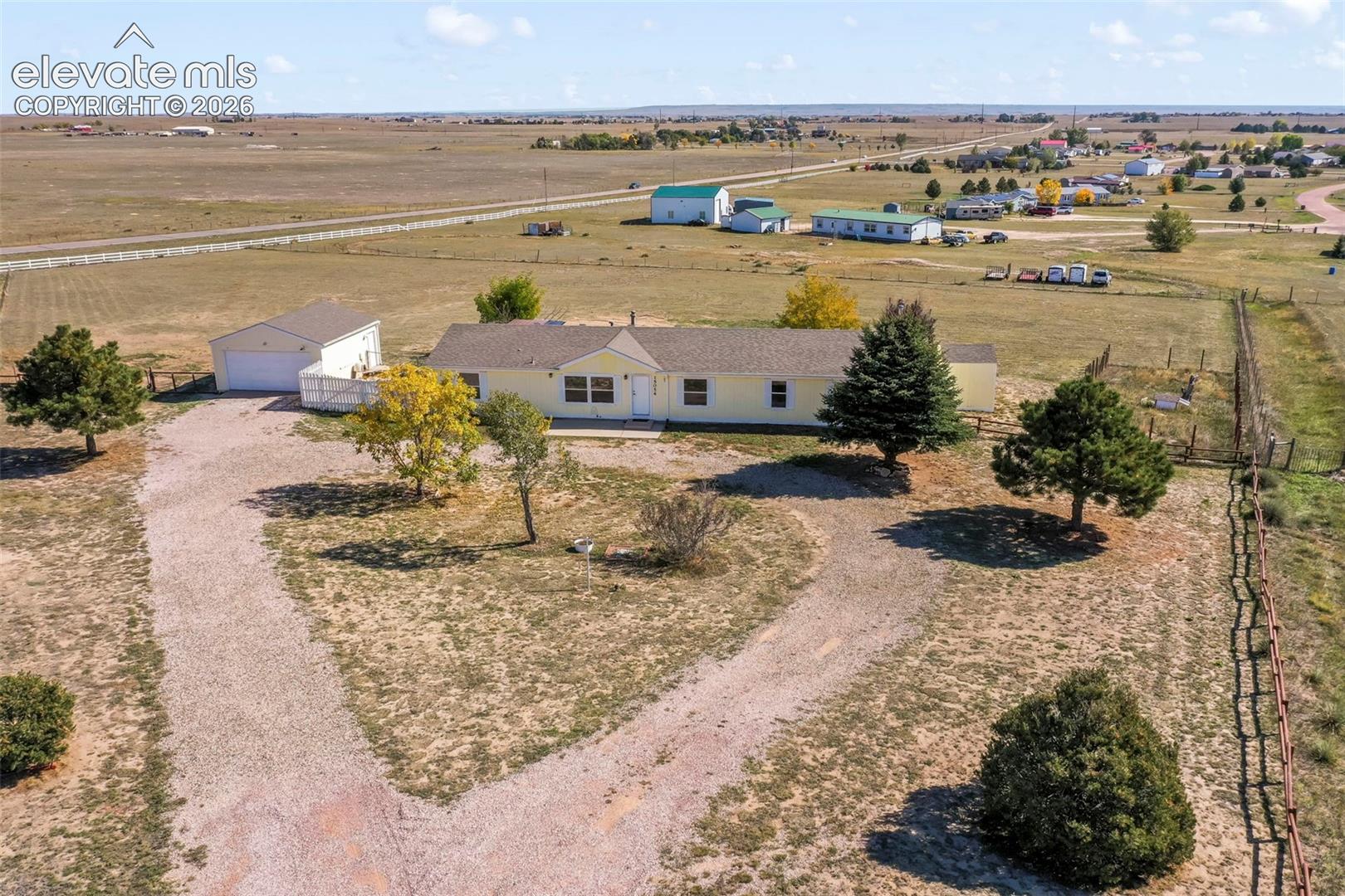 Ranch-style residence with an attached garage, featuring a gravel driveway and surrounding open landscape