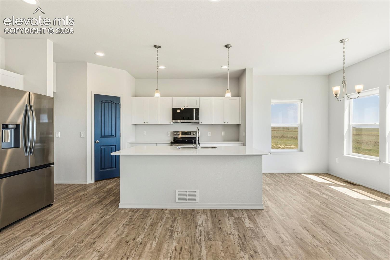Open-concept kitchen and dining area featuring wood-finish flooring, white cabinetry, a large kitchen island with pendant lighting, stainless steel appliances, and multiple windows