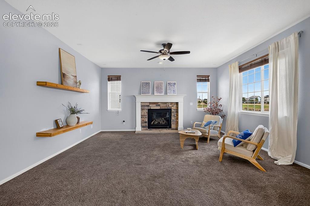 Stone-faced fireplace with a white mantel, ceiling fan with integrated lighting, two built-in floating shelves, and multiple windows