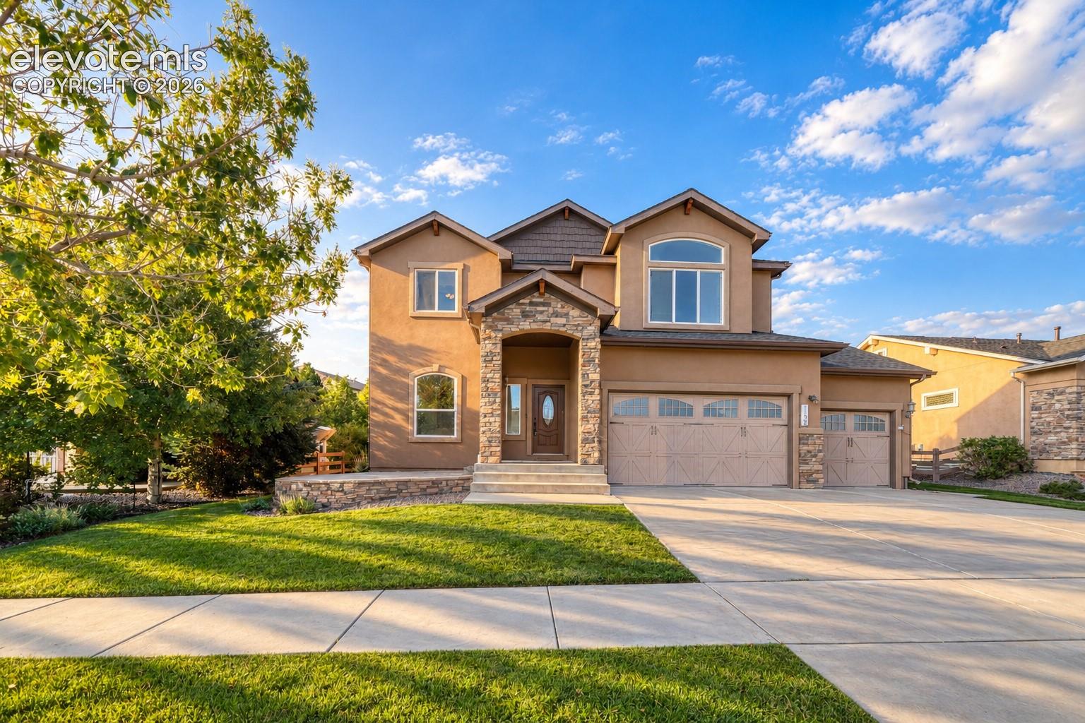 Stucco exterior with stone accents, arched entry, multiple garages, arched window, and mature landscaping