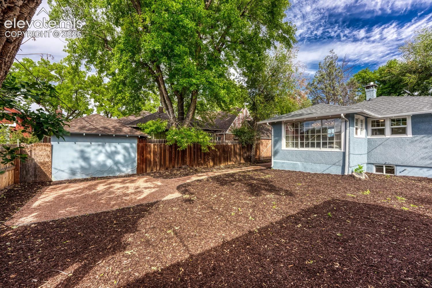 Exterior stucco finish, large picture windows, wood fencing, detached garage, and mature trees