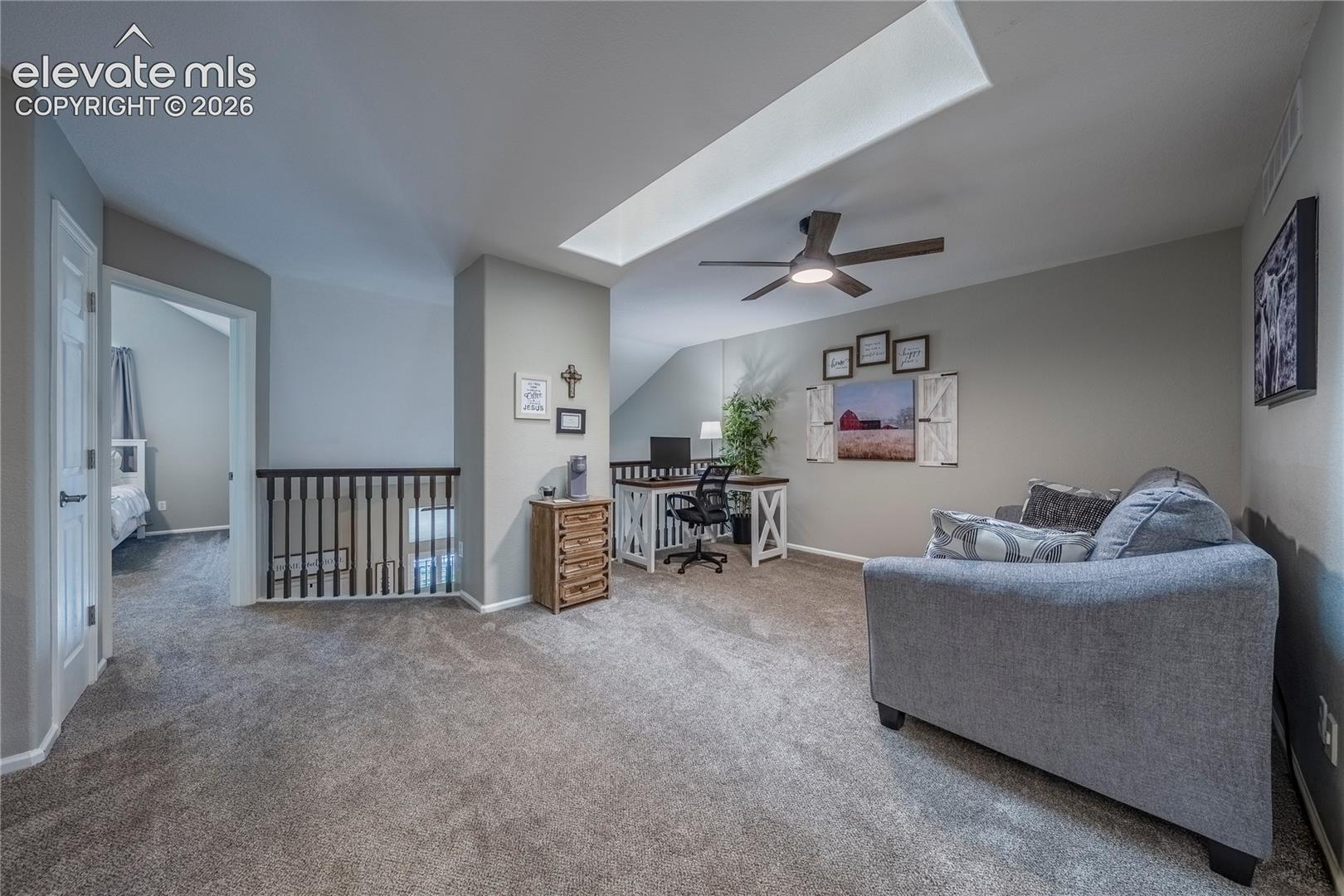 Open-concept interior featuring a vaulted ceiling with a rectangular skylight, a central ceiling fan with integrated lighting, and a metal-spindle railing